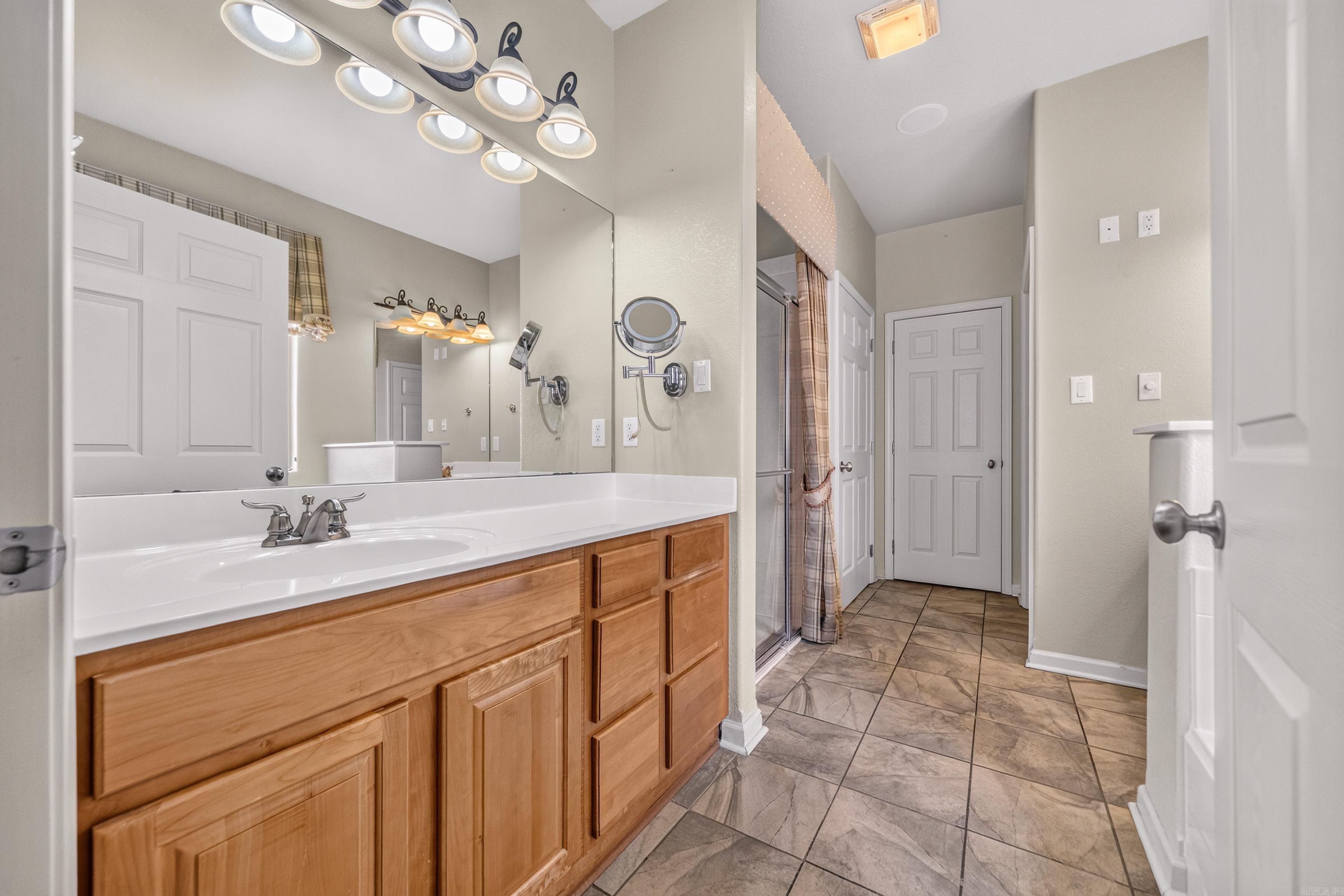 Bathroom with a long wood vanity, expansive mirrors, and a glass-enclosed shower.