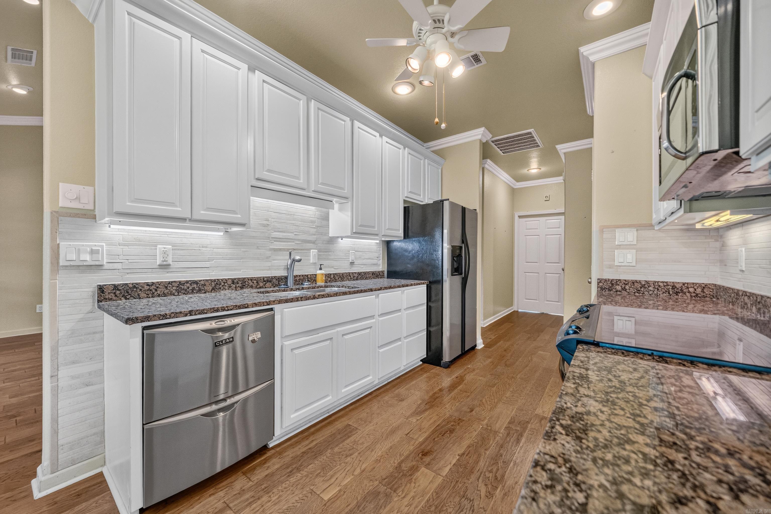 Kitchen with white cabinets, stone counters, stainless steel appliances, and wood flooring.