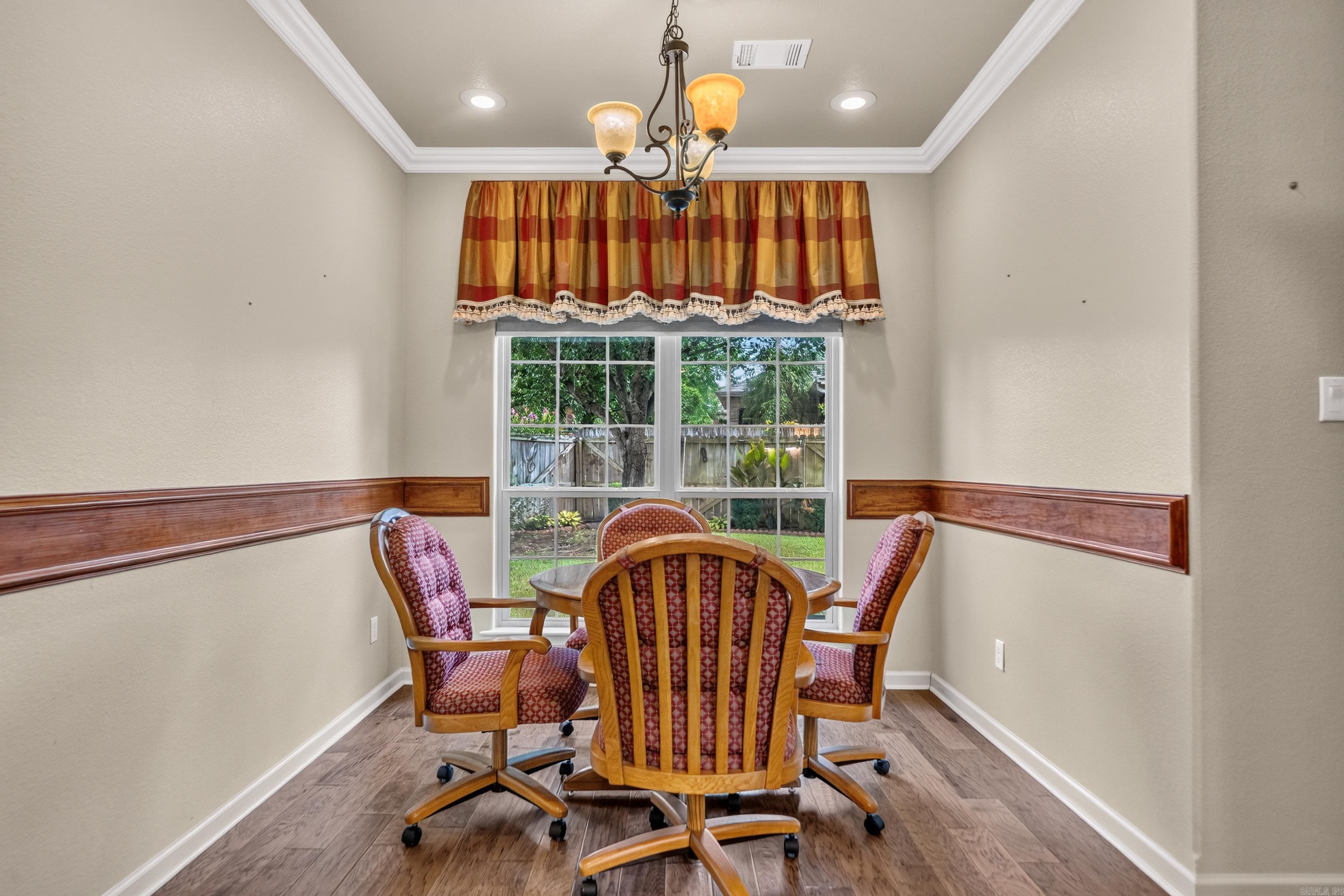 Dining room with four red-patterned chairs around a wooden table beside a large window.