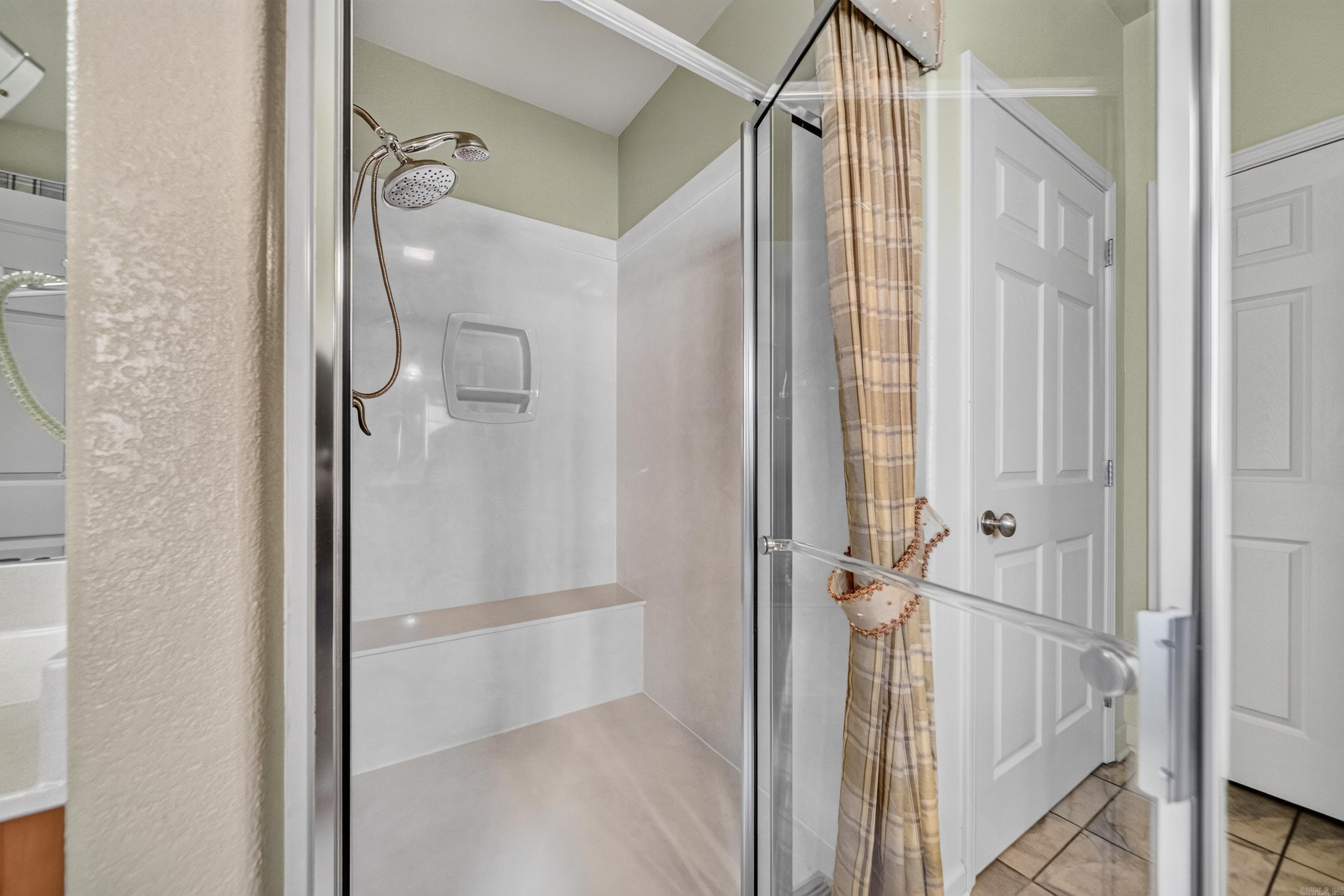 Walk-in shower with glass doors, a built-in bench, dual showerheads, and a gathered plaid curtain.