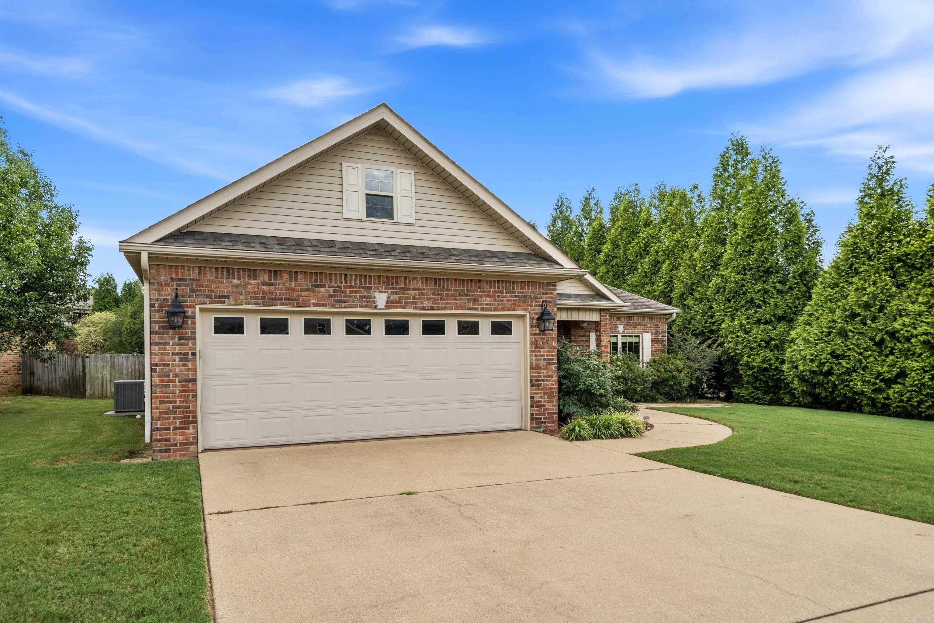 Brick house with a two-car garage, broad driveway, and tall evergreen trees.