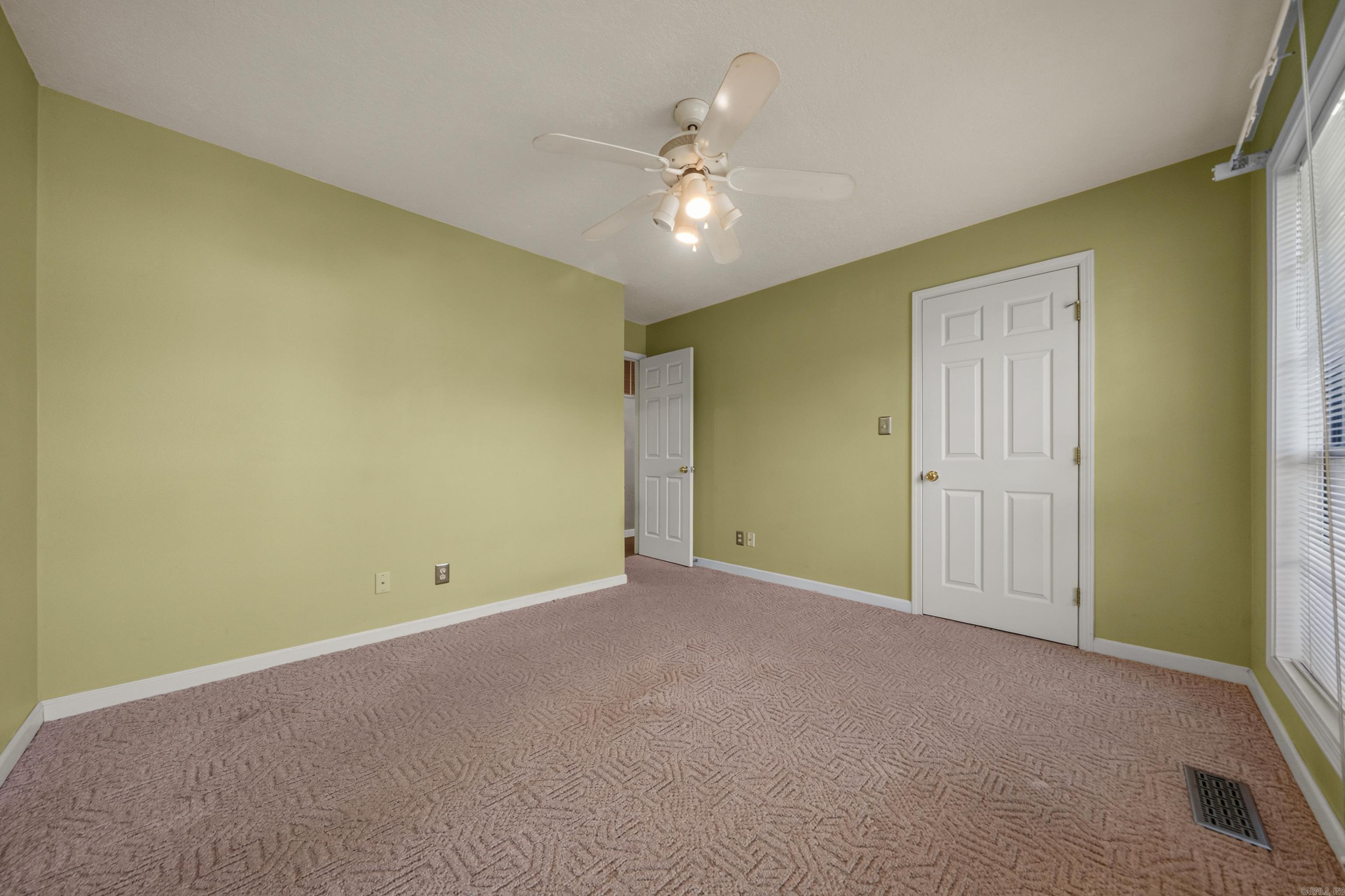Empty bedroom with pale green walls, patterned carpet, ceiling fan, and tall windows.