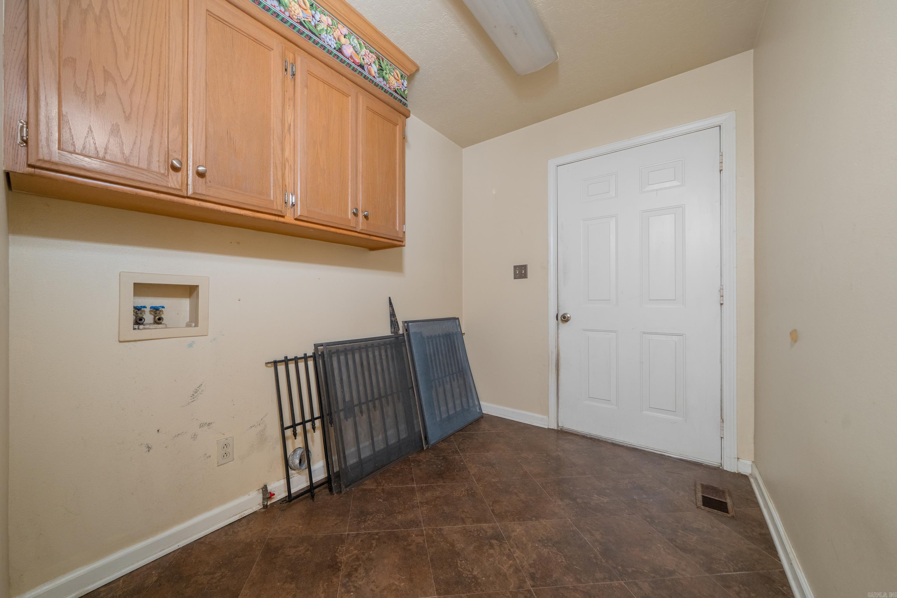 Laundry room with wood cabinets, washer hookups, and window screens leaning against the wall.