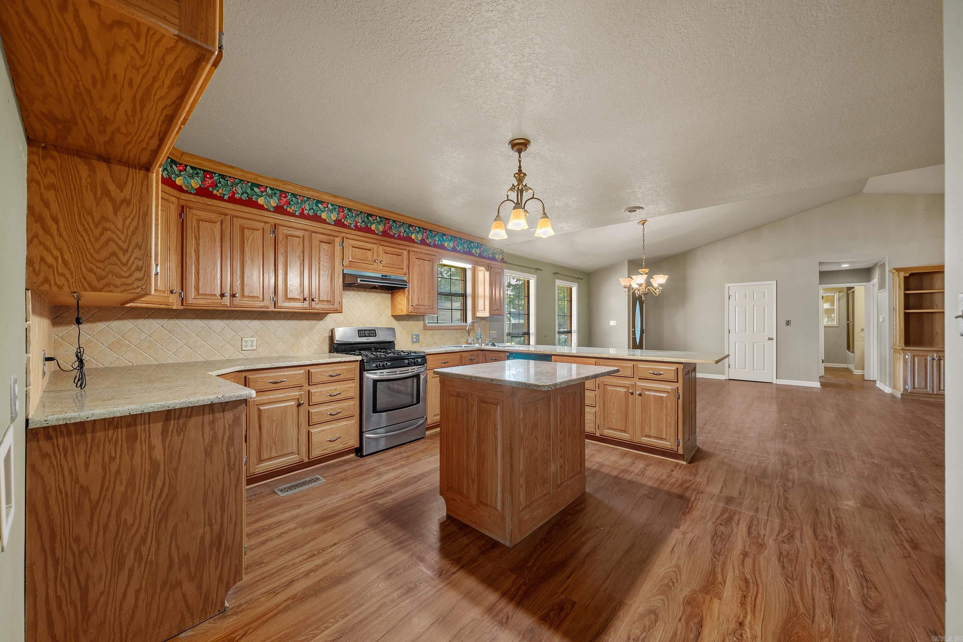 Kitchen with warm wood cabinetry, a central island, stainless steel range, and wood-look flooring.