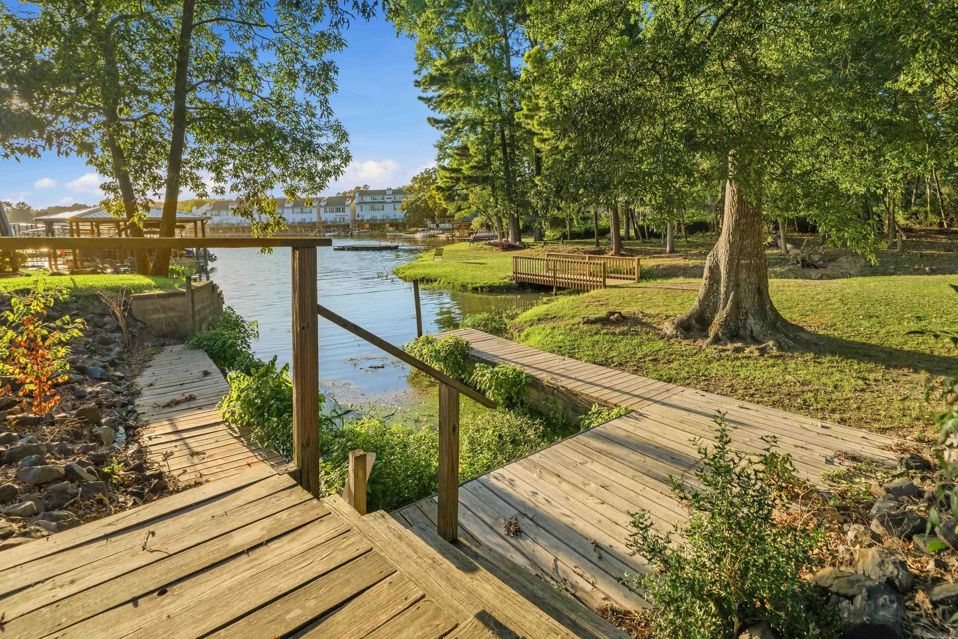 Wooden boardwalks beside a tree-lined cove, with a small landing and buildings across the water.