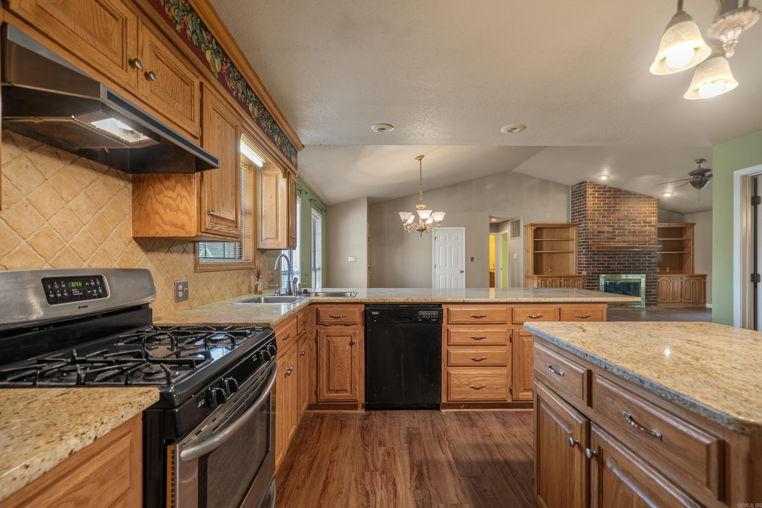 Kitchen with wood cabinets, granite counters, gas range, and a view of the brick fireplace.