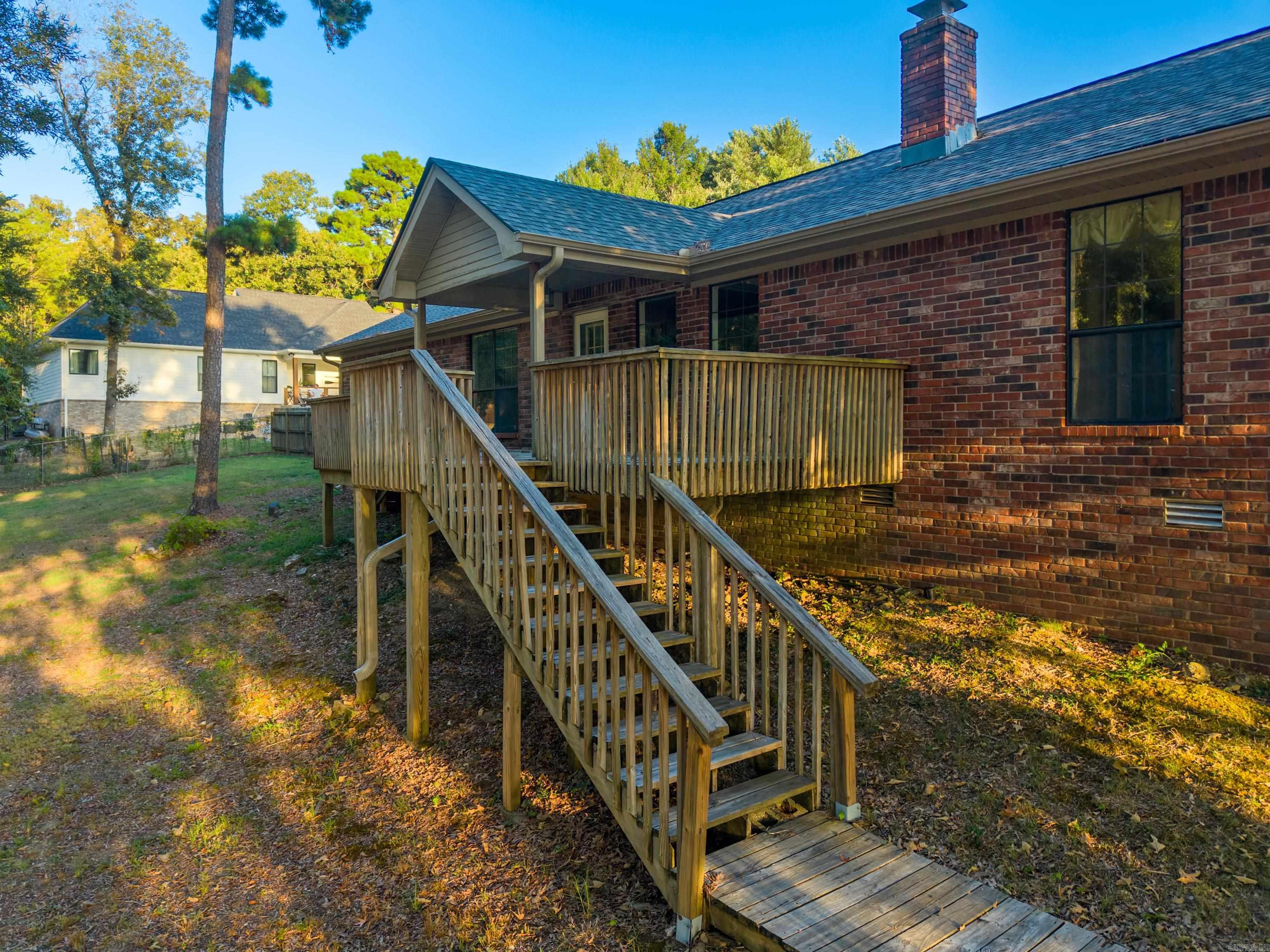 Red-brick home with a raised wooden deck and long staircase leading to the yard.