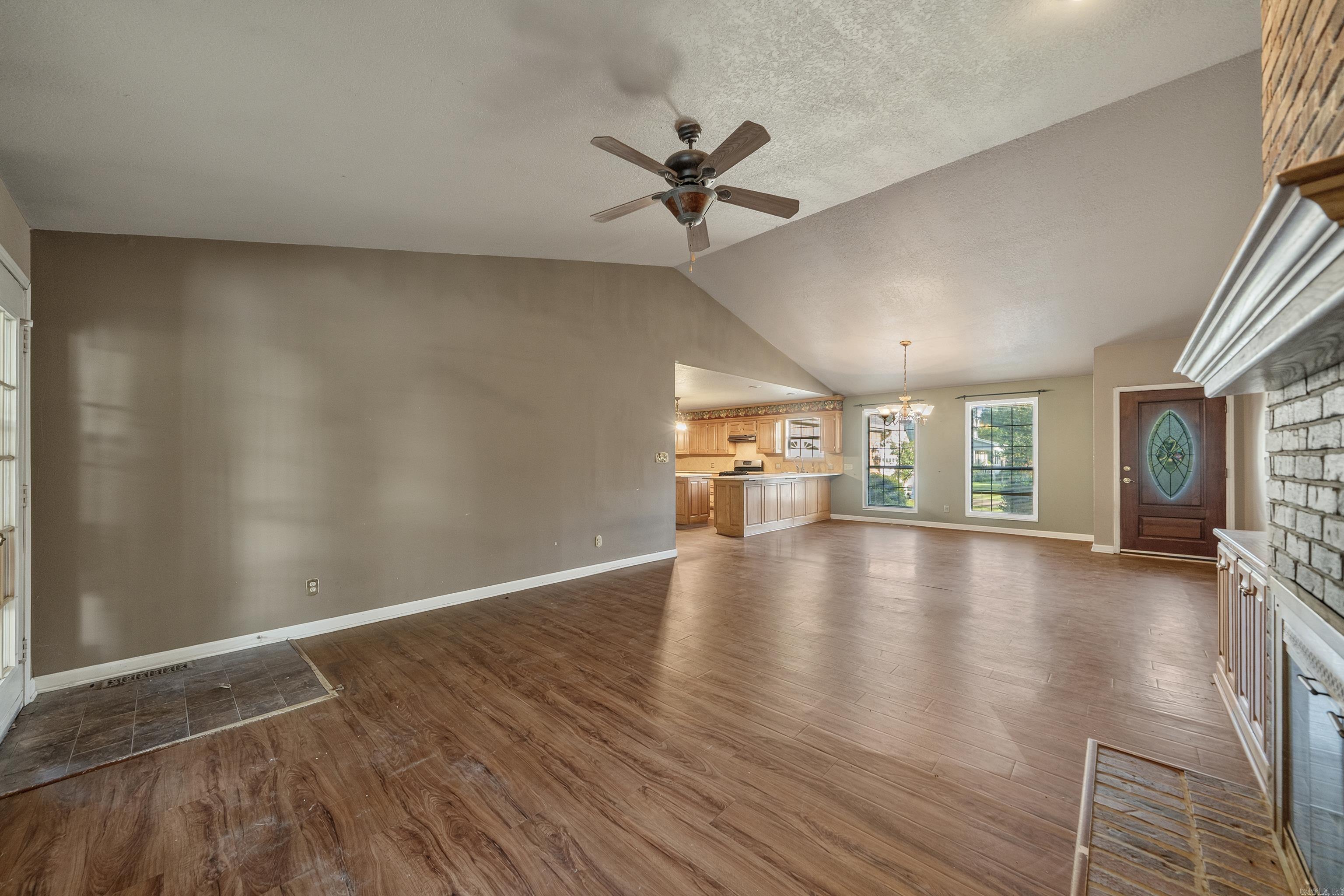Open living and dining area with wood-look floors, vaulted ceiling, and adjoining kitchen.