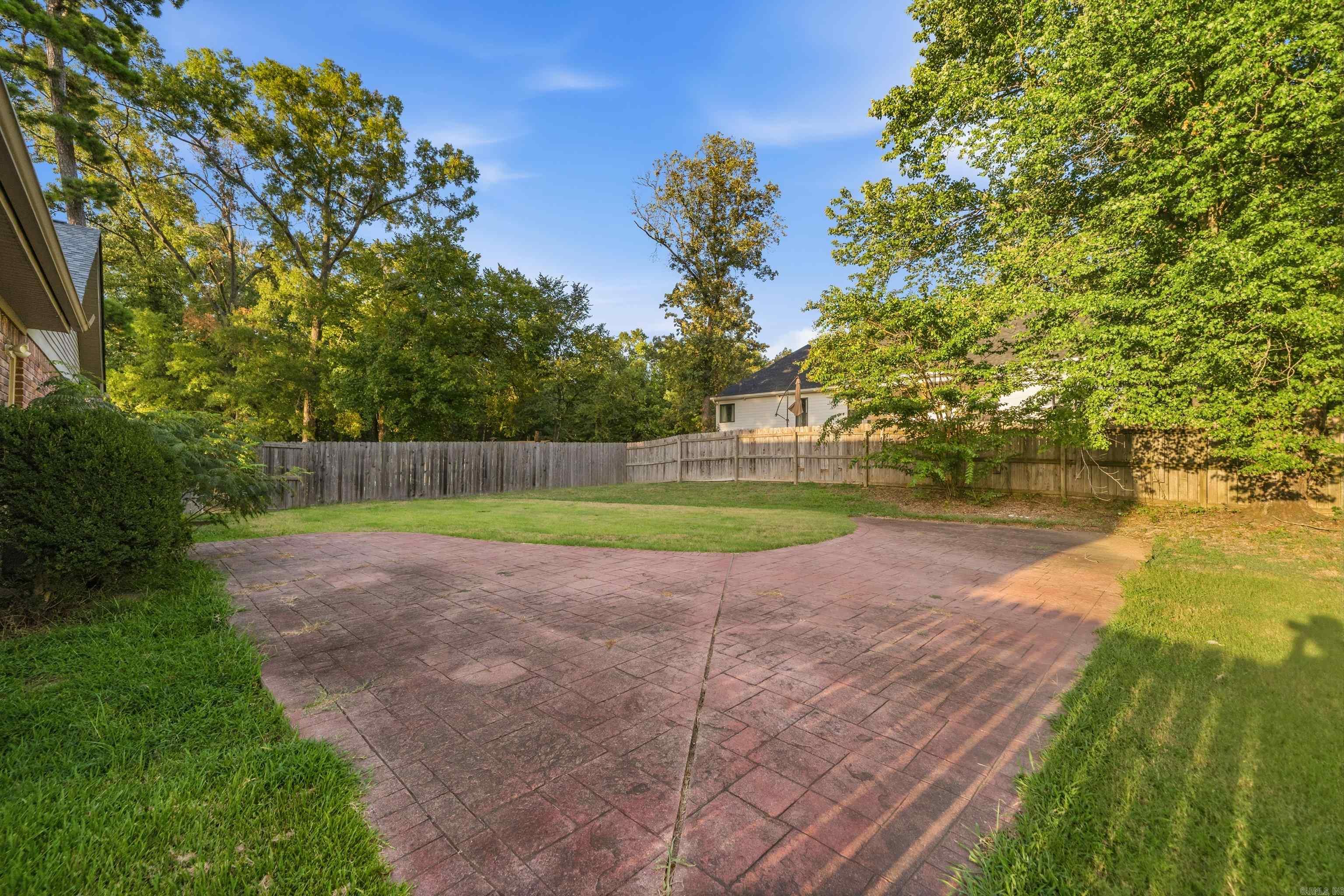 Fenced backyard with a broad stamped-paver patio, lawn, and mature trees.