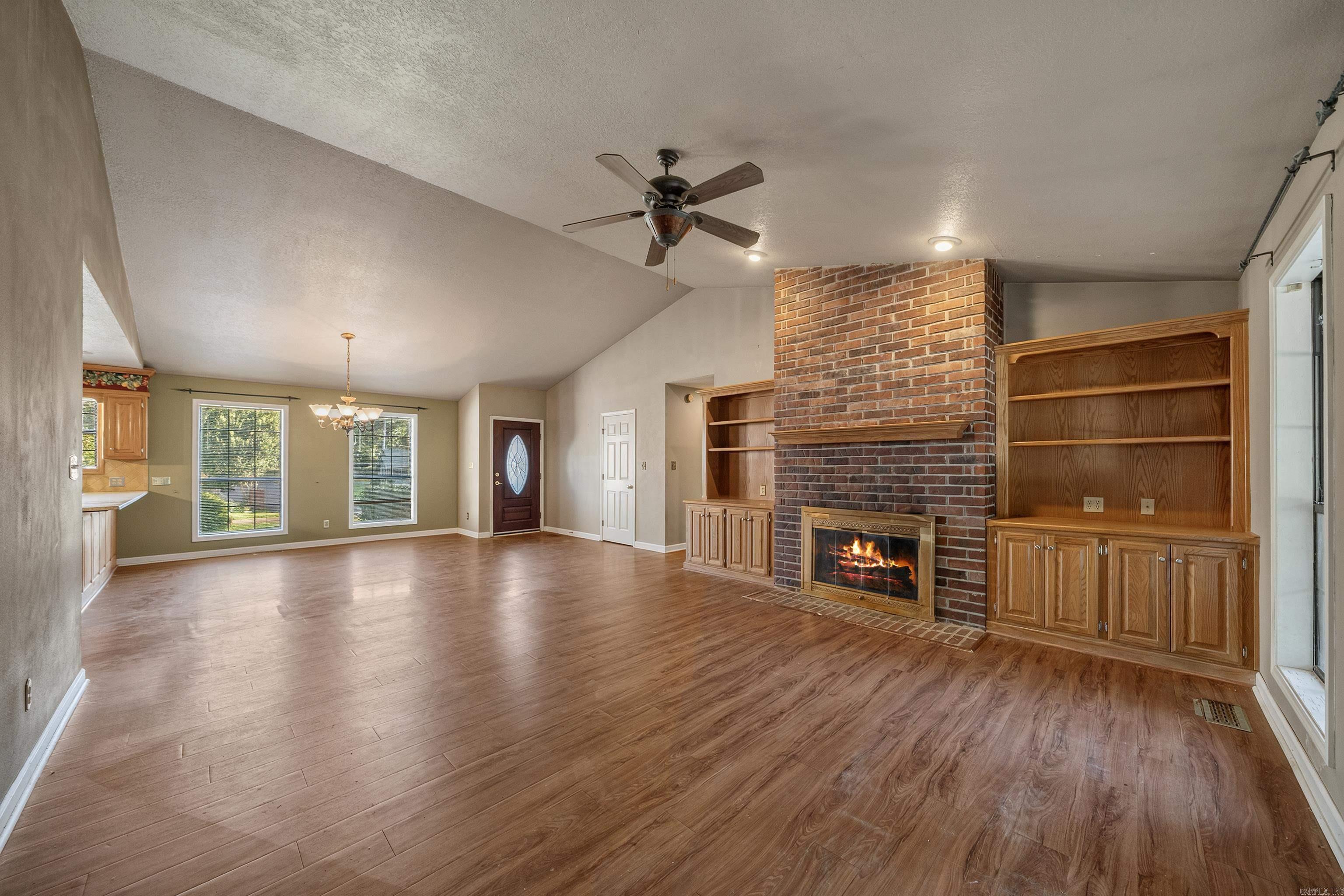 Vacant living room with a brick fireplace, built-in wooden shelving, and brown plank flooring.