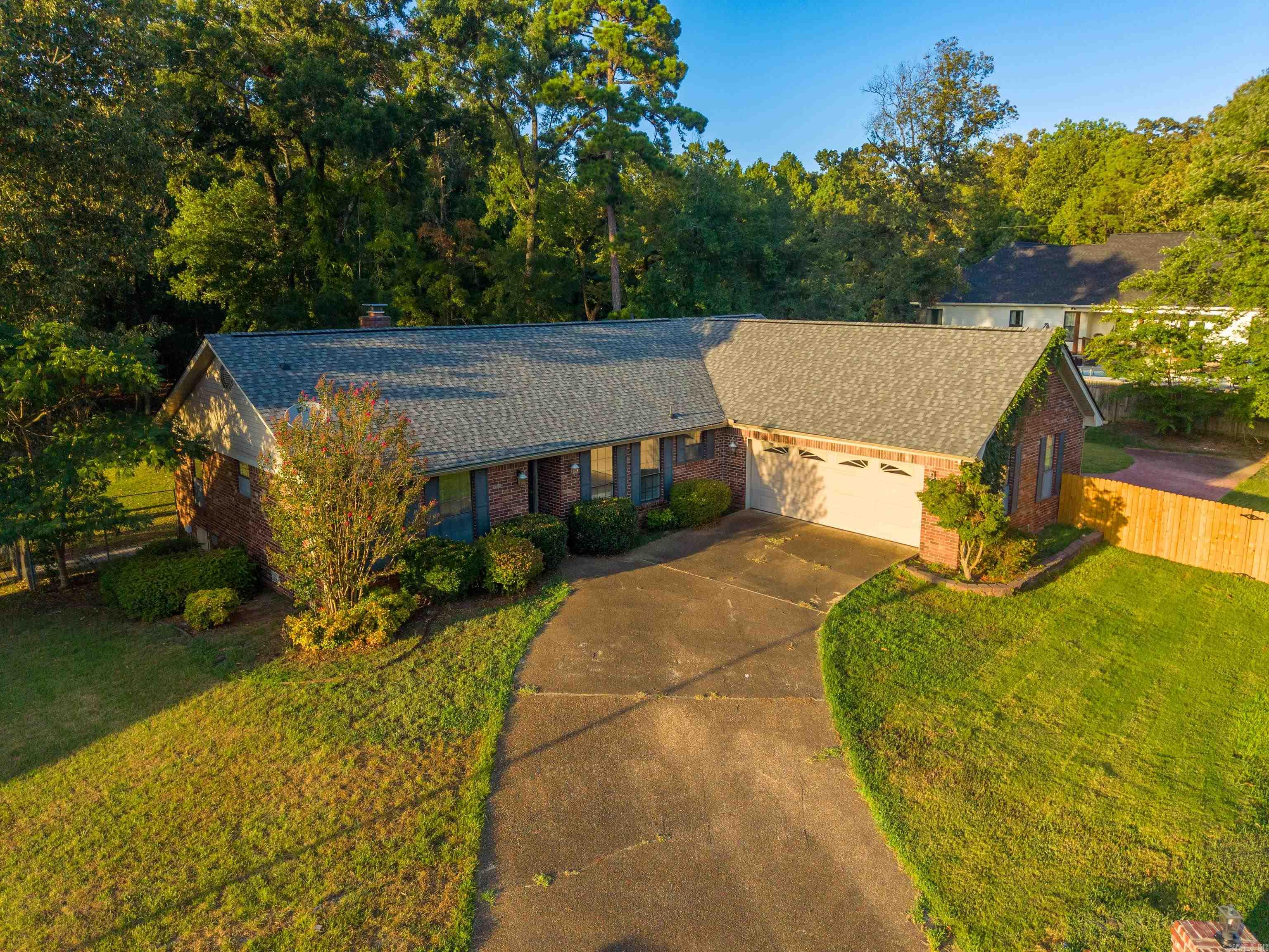 Brick house with a two-car garage and curved driveway, surrounded by mature trees.