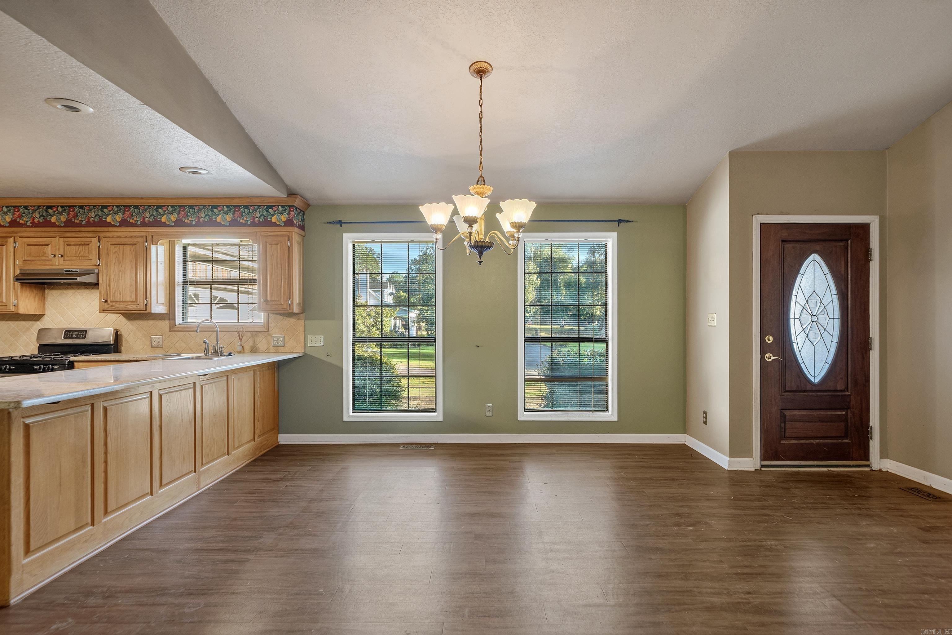 Kitchen and dining area with light wood cabinets, water visible through two windows, and a decorative glass front door.