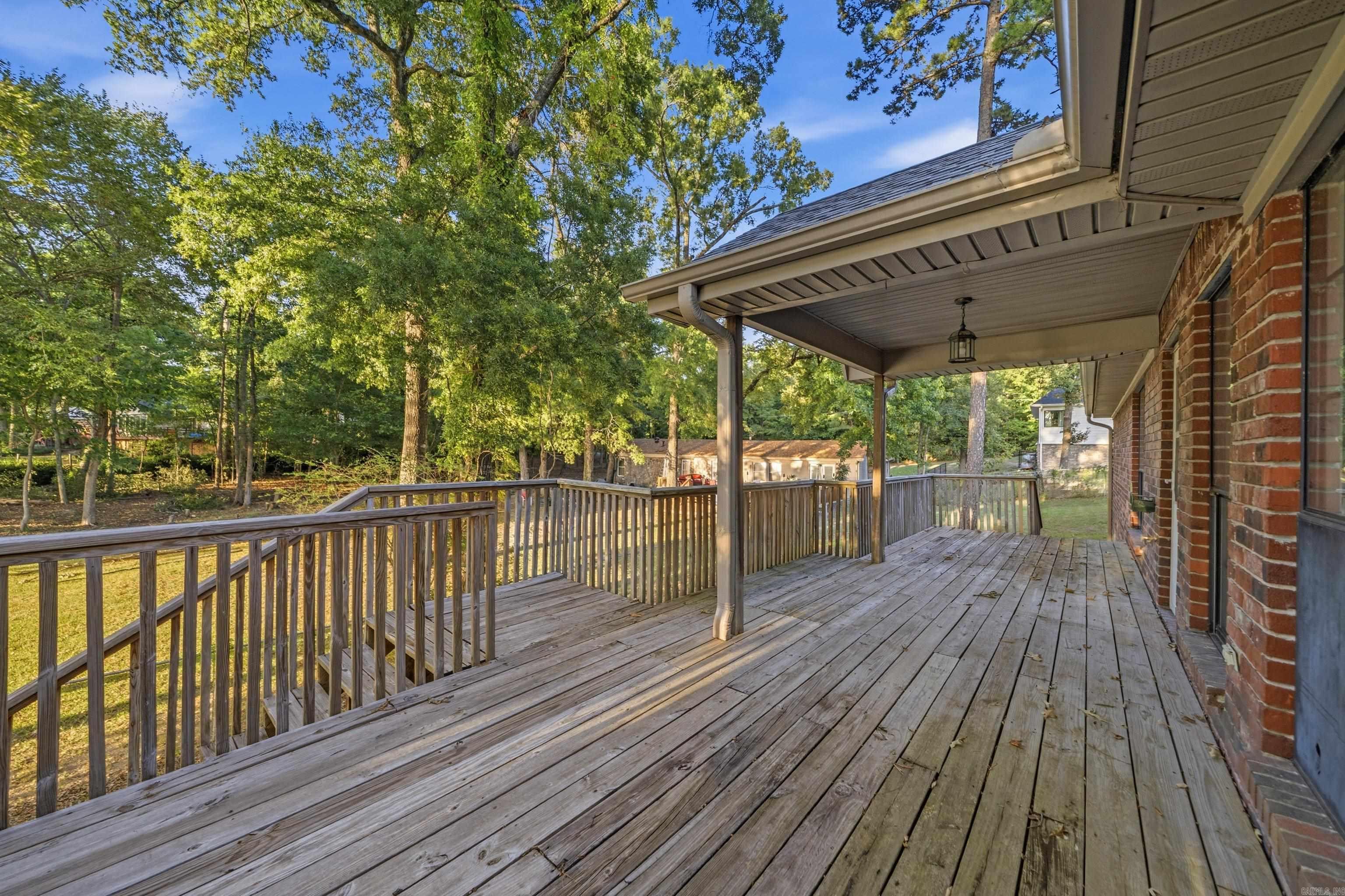 Wood deck beside a brick house, partly covered and overlooking a leafy wooded yard.