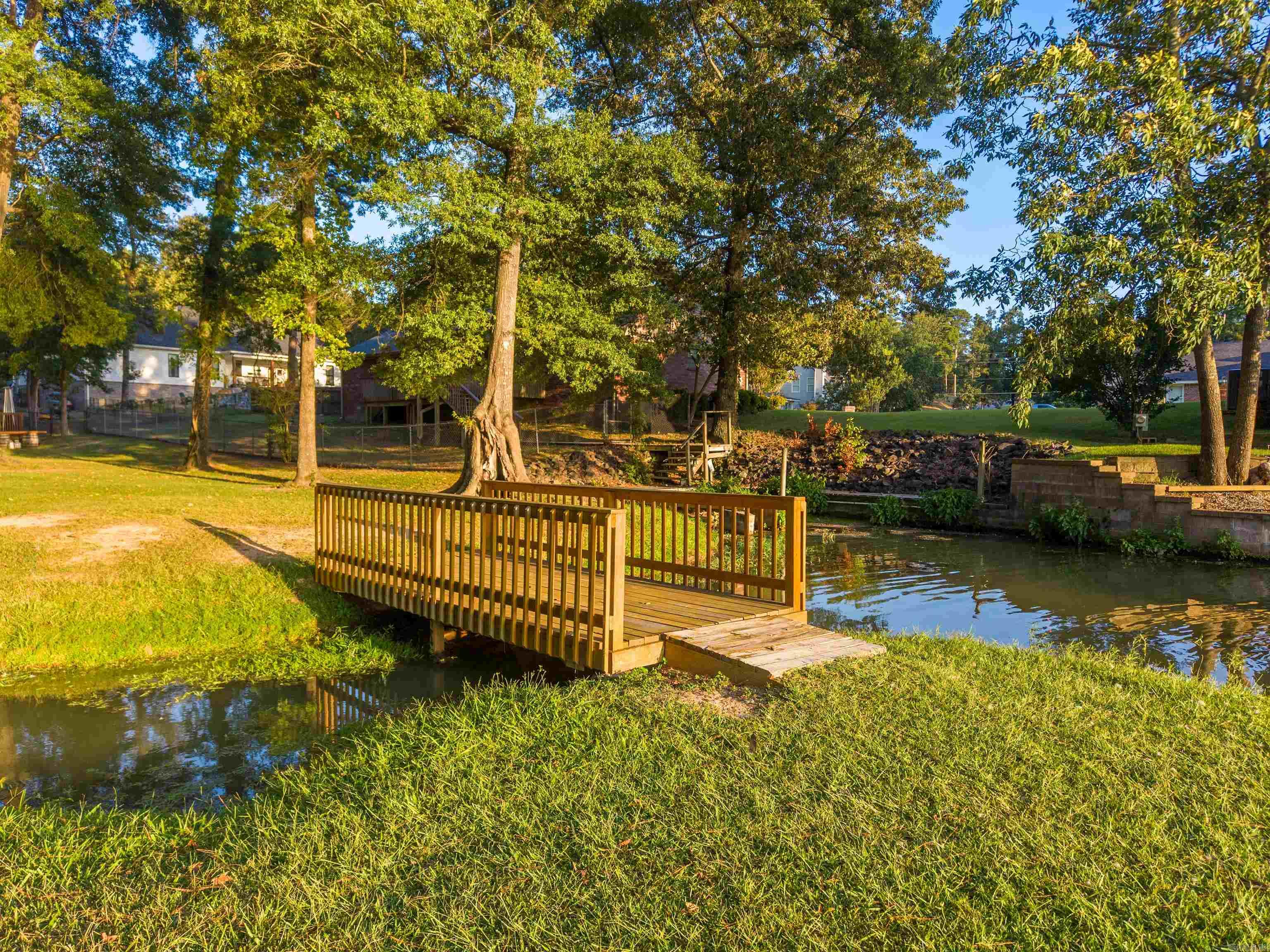 Waterfront yard with a wooden footbridge over a narrow channel beneath mature trees.