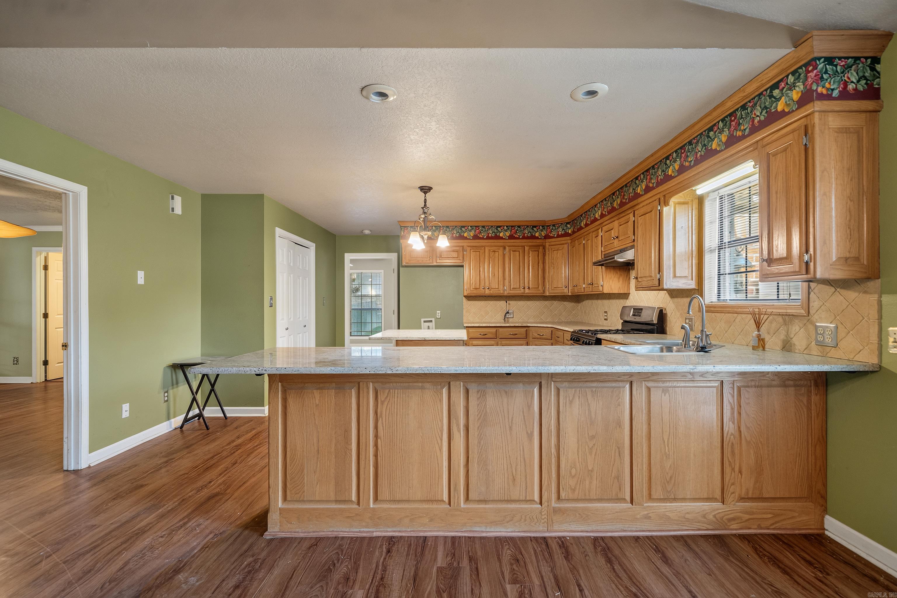 Kitchen with honey-toned wood cabinets, a large stone-topped breakfast bar, and green walls.