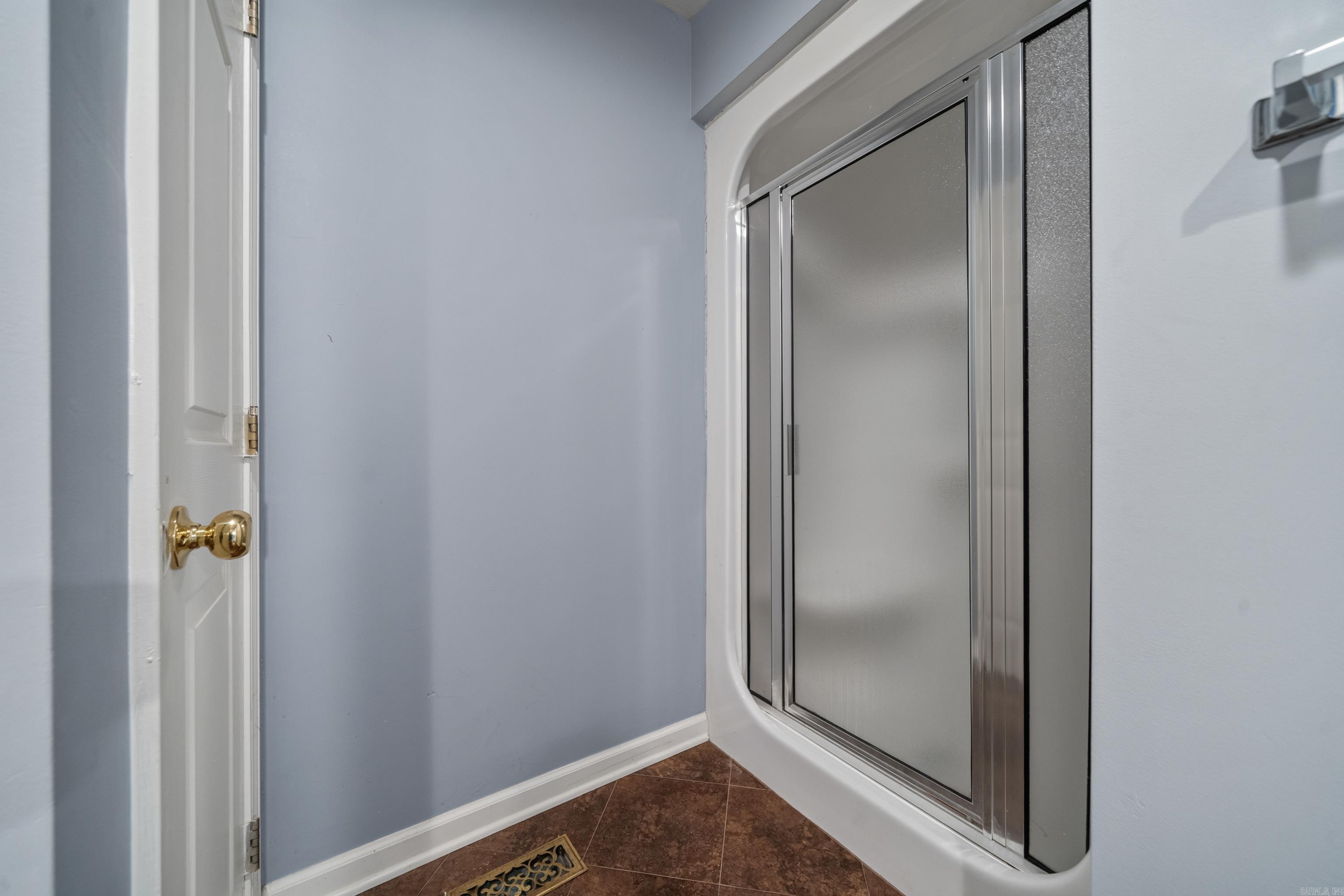 Bathroom shower with frosted sliding glass doors, blue walls, and brown tile floor.
