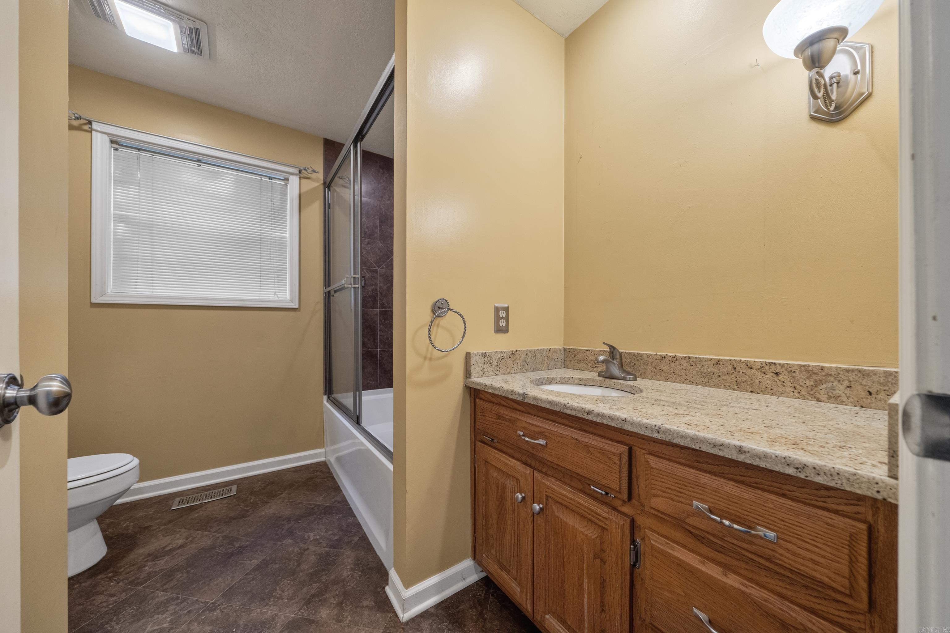 Bathroom with a long wood vanity and stone countertop beside a glass-enclosed tub and shower.