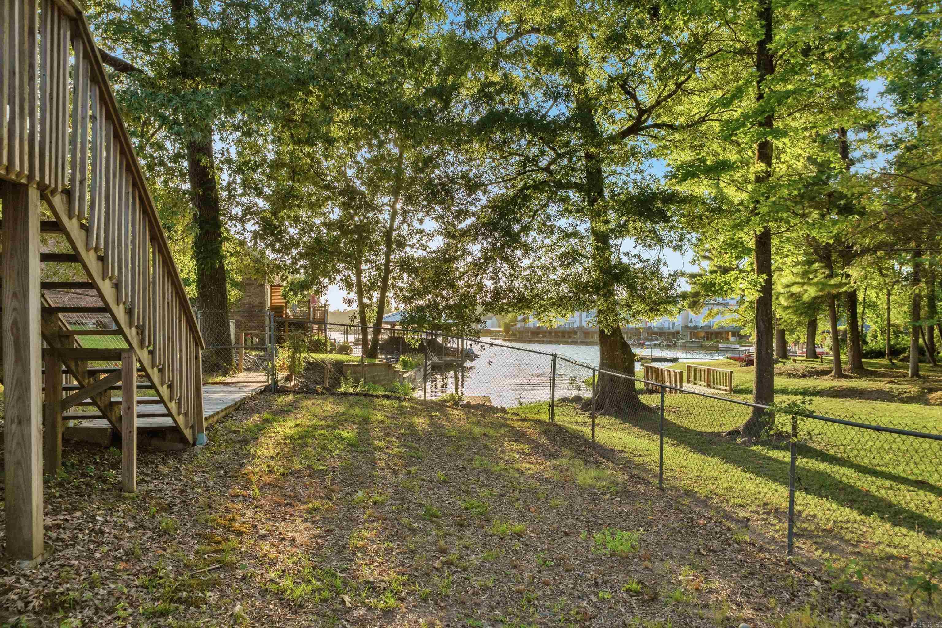 Shaded waterfront yard with deck stairs, mature trees, and a fenced shoreline.