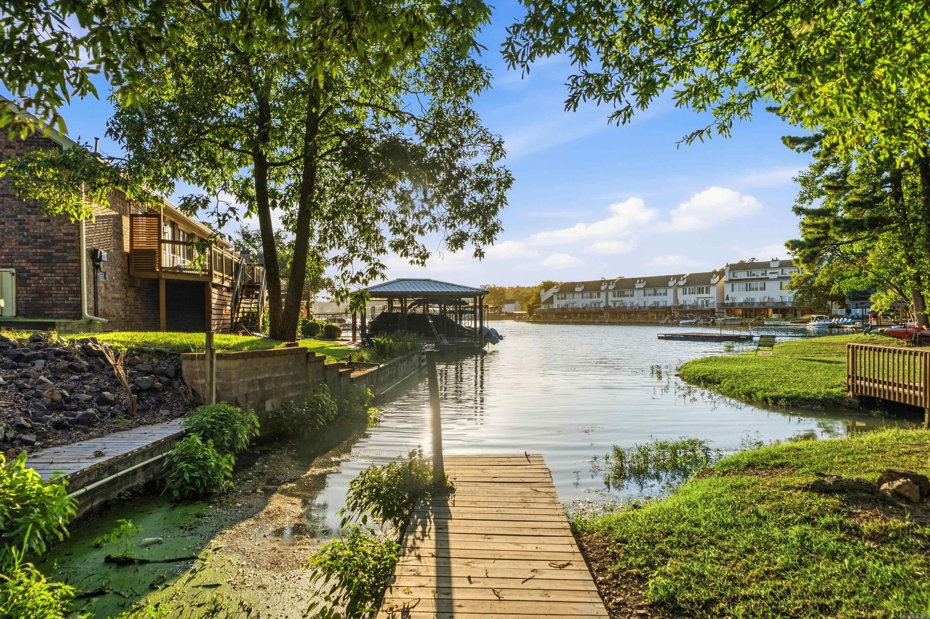 Waterfront homes and a covered boat slip across a cove, viewed from a wooden dock.