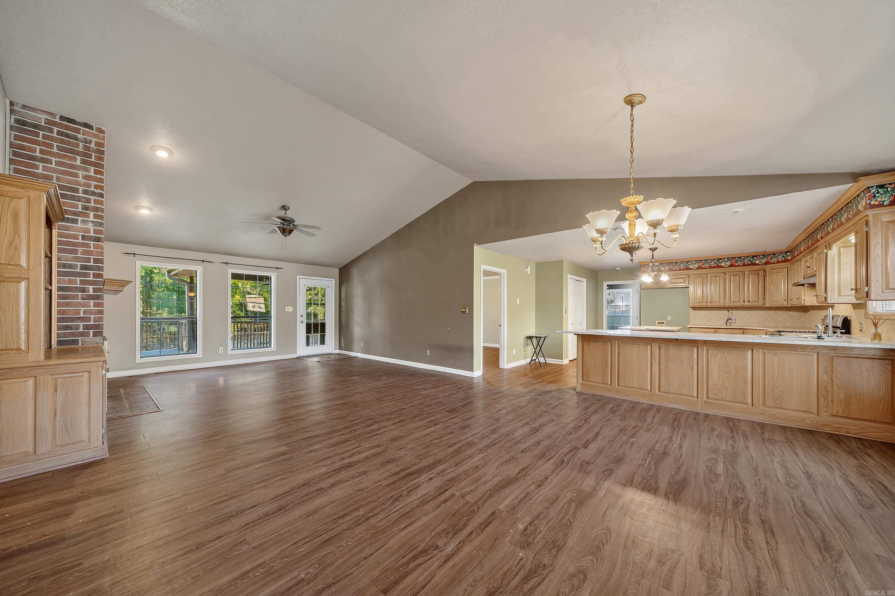 Open living area and kitchen with vaulted ceiling, brick accent wall, and wood cabinetry.