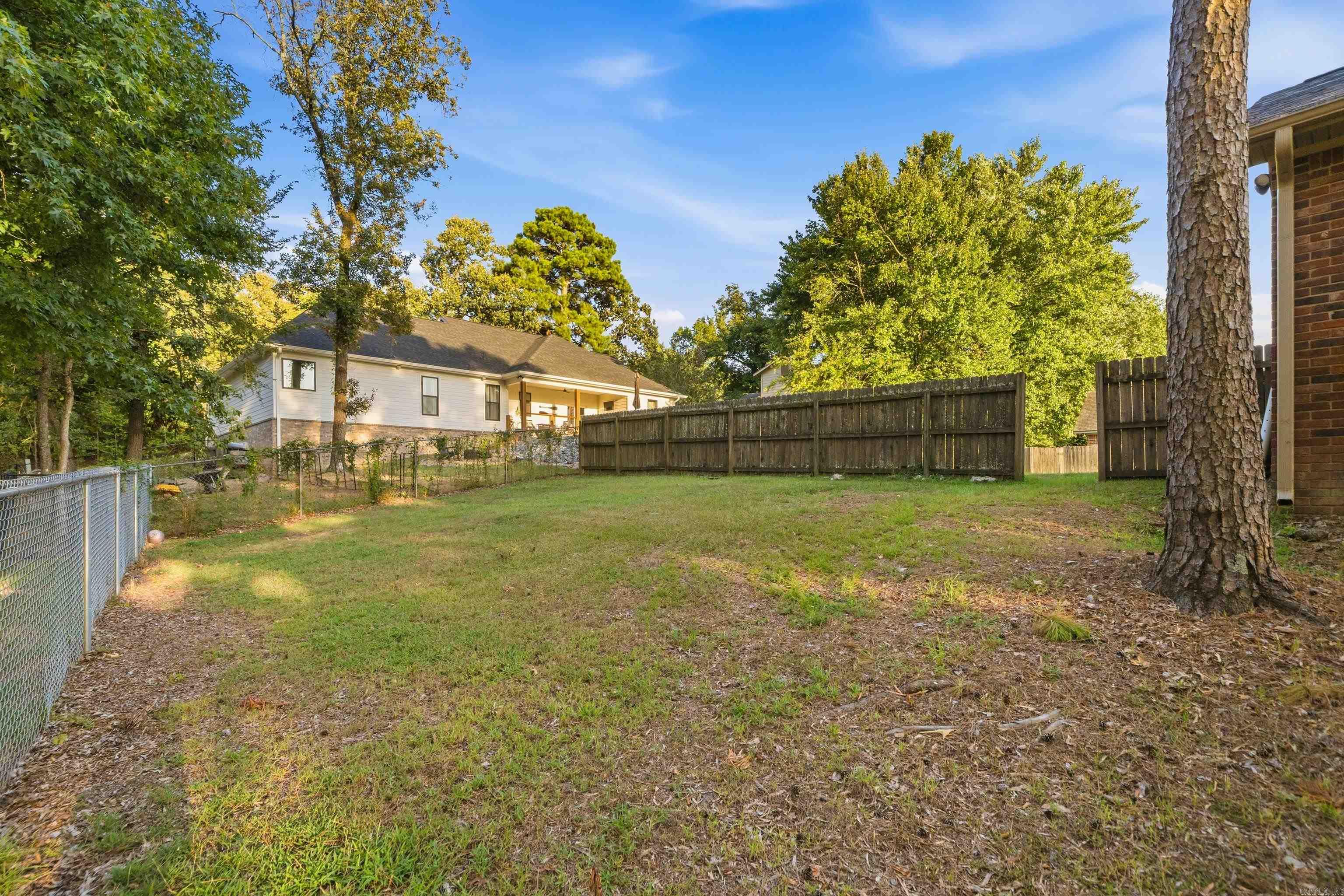 Backyard with a grassy lawn, wooden privacy fence, chain-link fence, and mature trees.