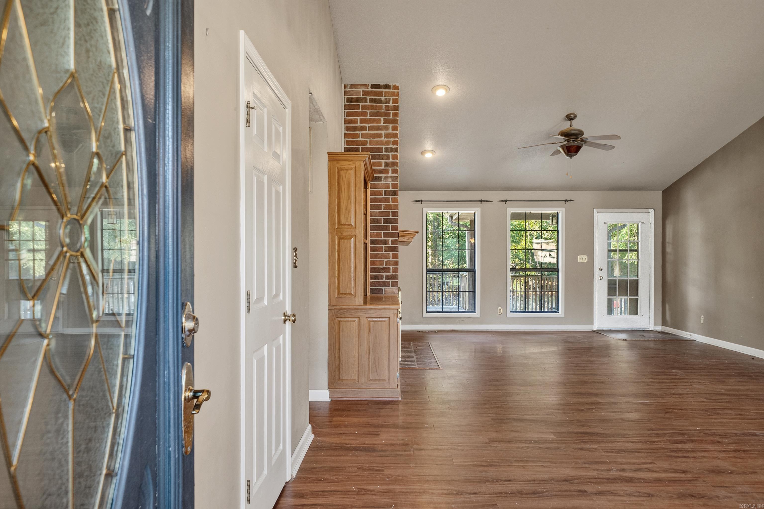 Empty living room with a brick fireplace wall, built-in wood cabinetry, and windows facing a deck.