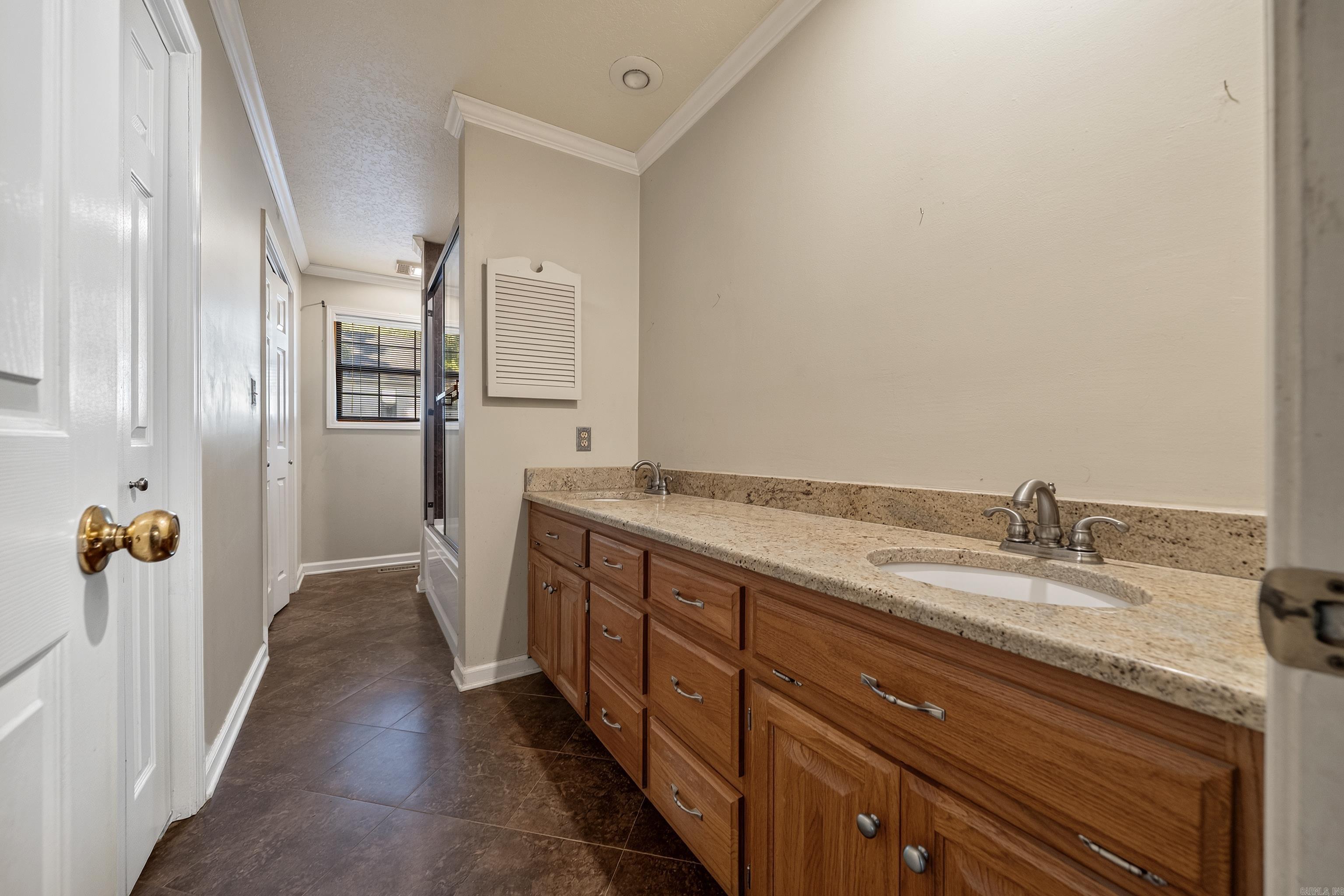 Bathroom with a long wood double vanity, stone countertop, and dark tile floor.