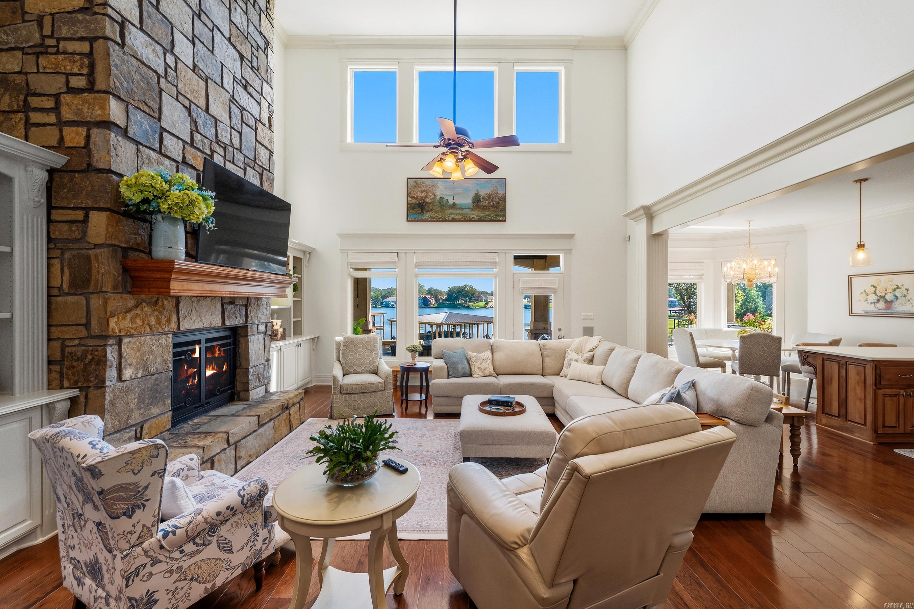 Living room with a tall stone fireplace, vaulted ceiling, and windows overlooking the water.