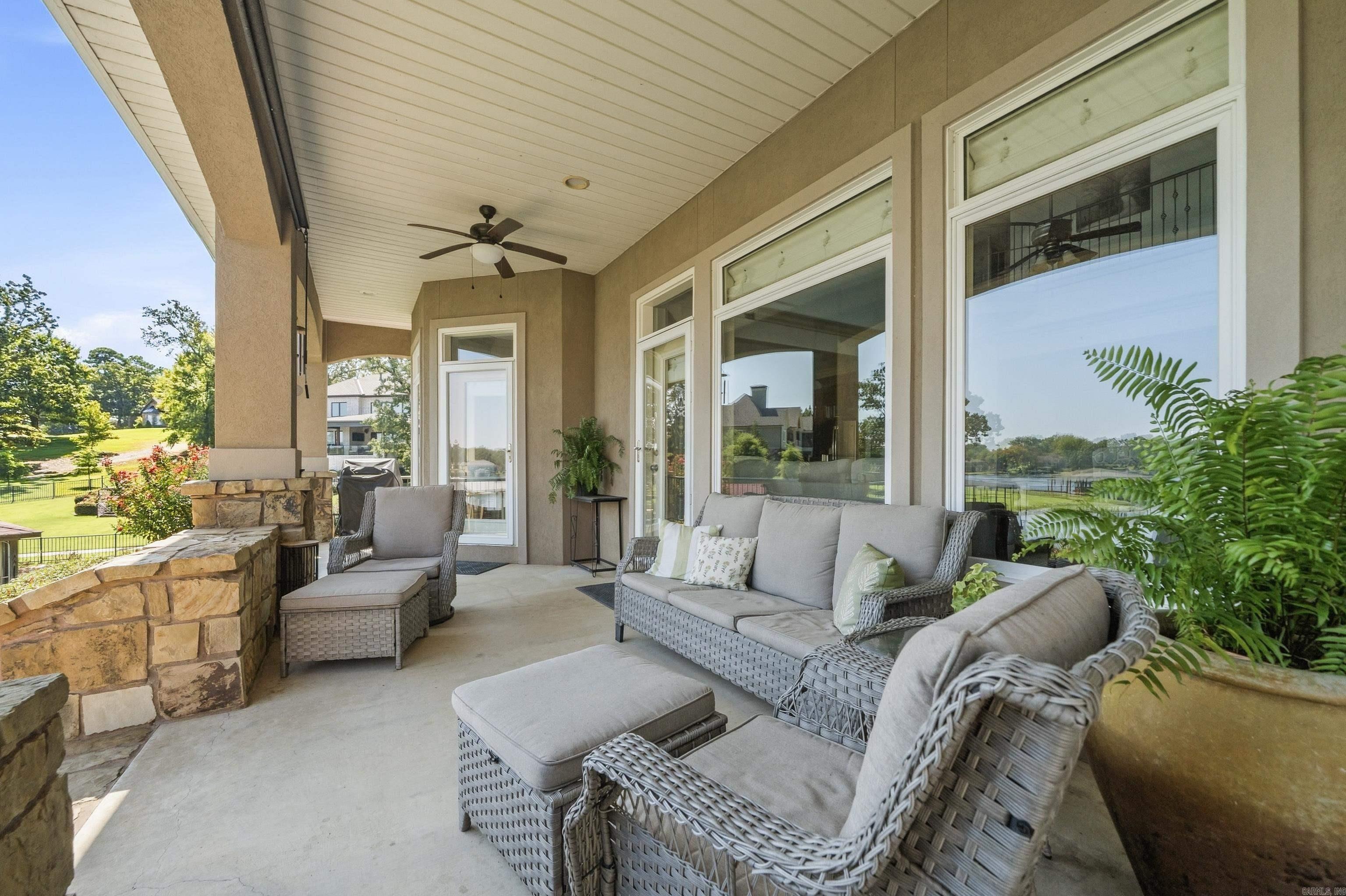 Covered patio with wicker seating and stone wall, overlooking a landscaped yard and lake.