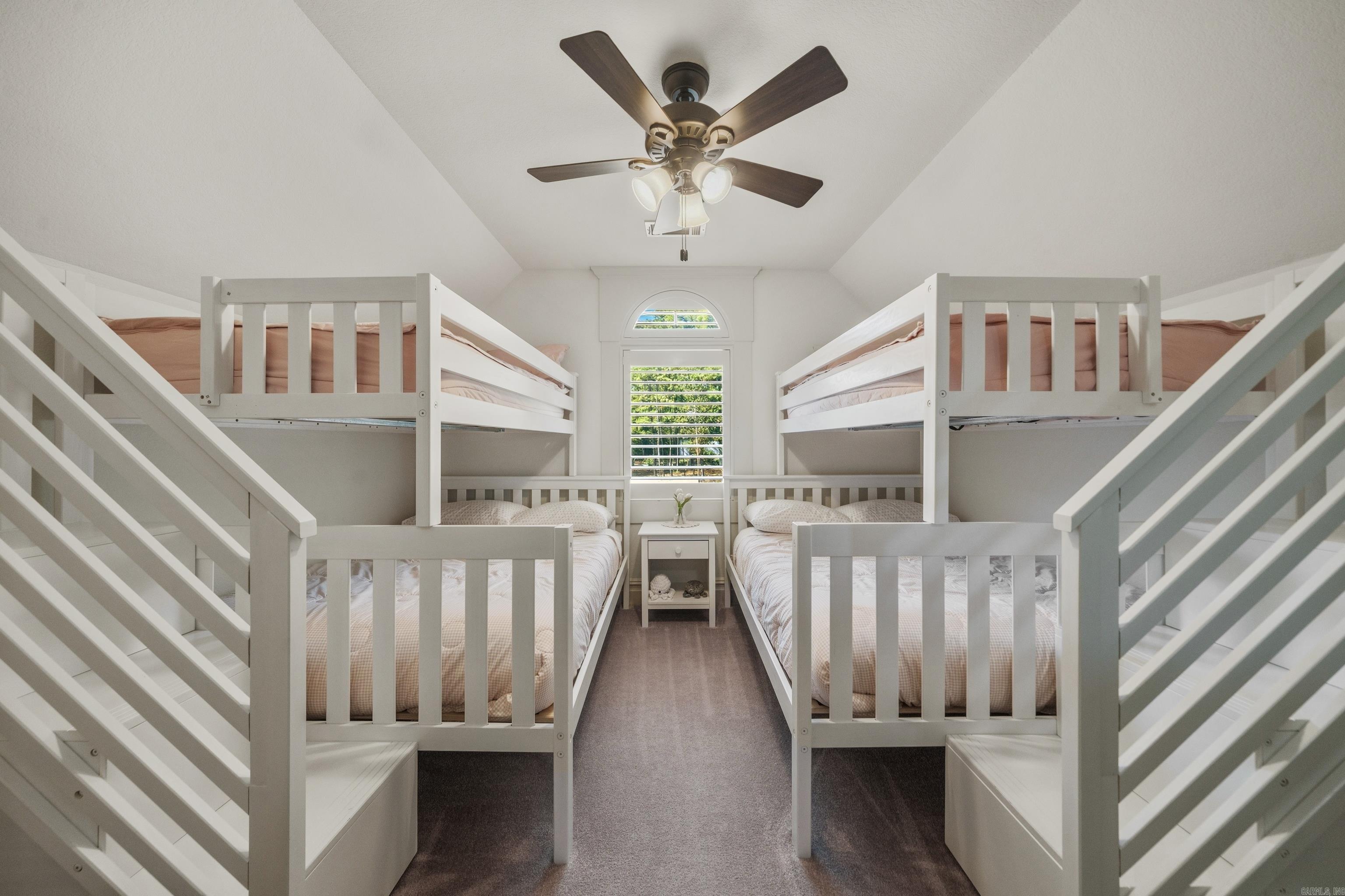 Bedroom with two white bunk-bed sets, built-in staircases, and a ceiling fan.