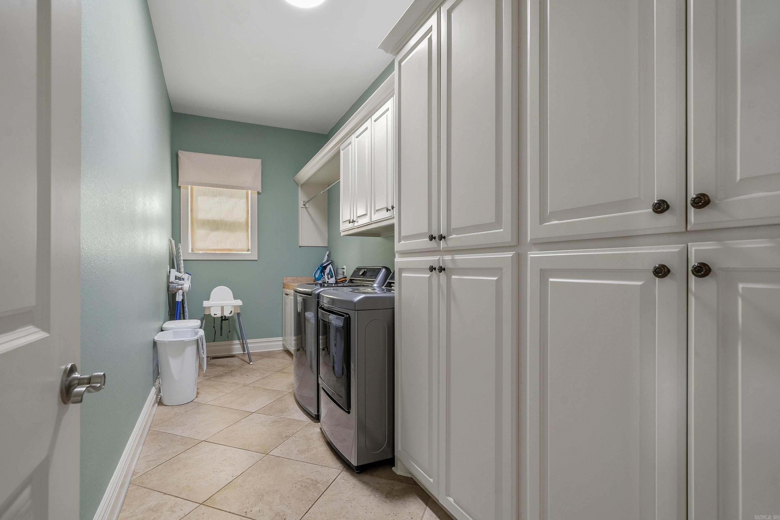 Laundry room with front-loading washer and dryer beneath extensive white built-in cabinets.