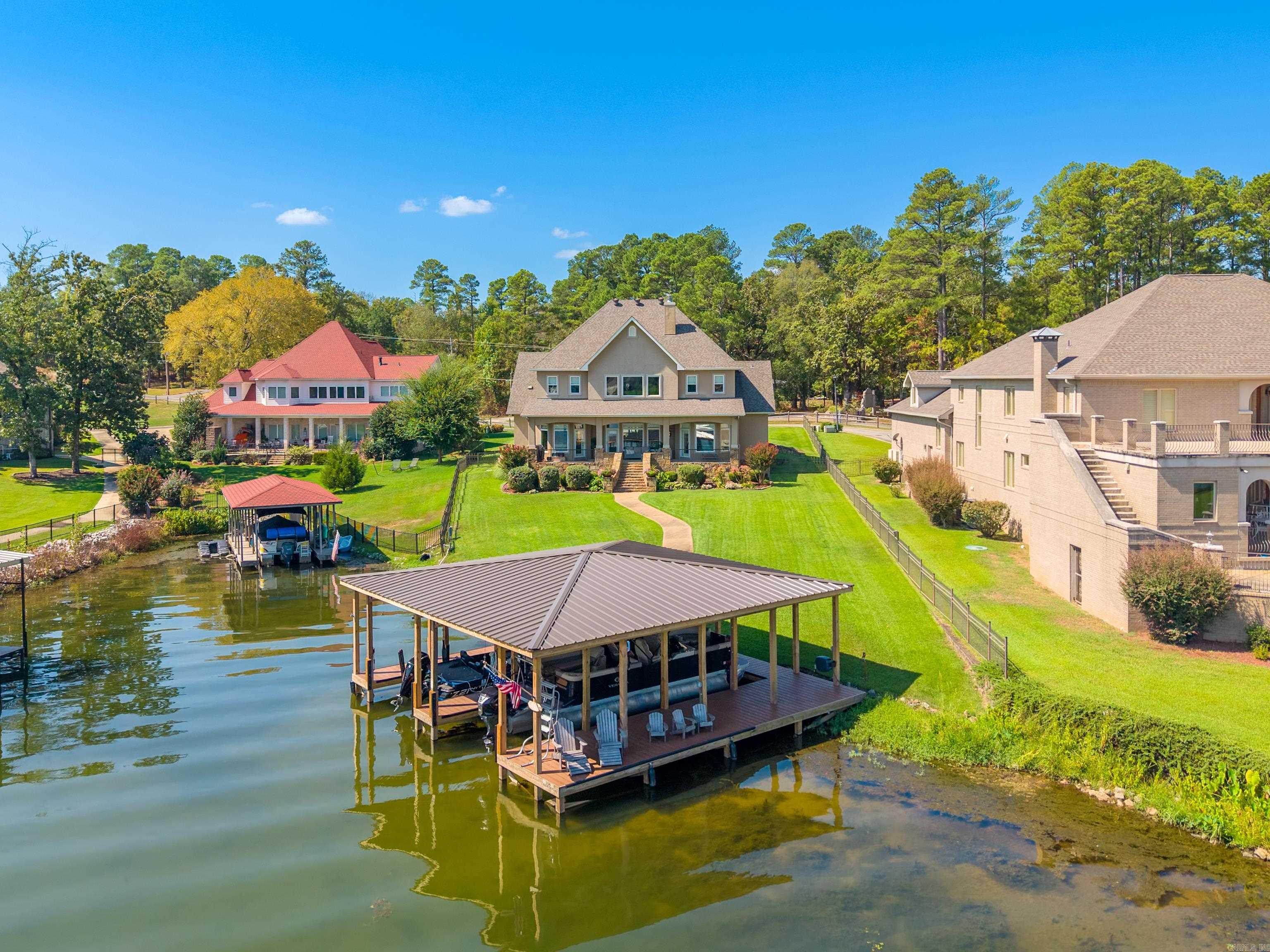 Aerial view of a lakeside home and covered dock beside a broad green lawn.