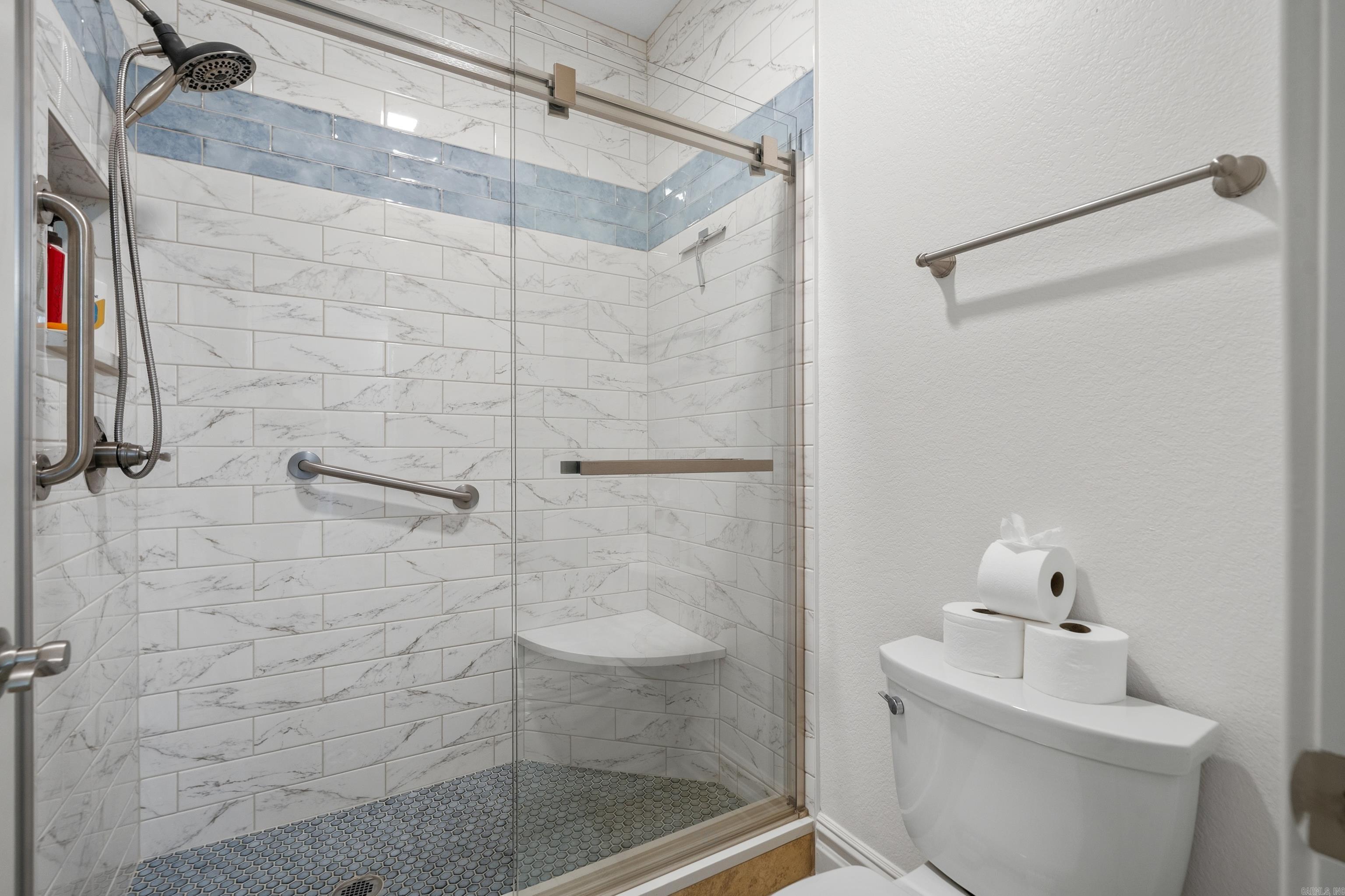Bathroom with a glass shower, blue tile accent, corner seat, and grab bars.