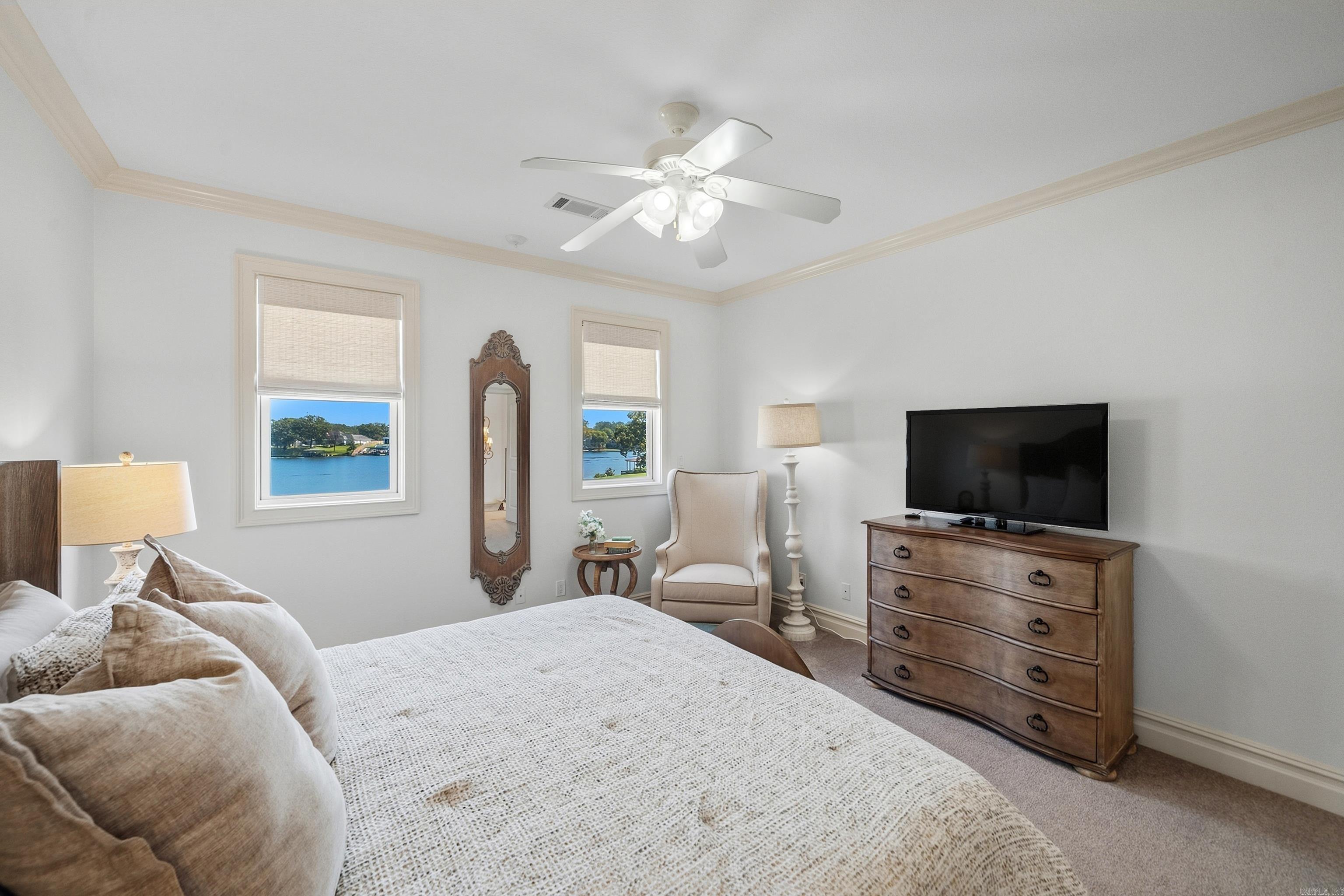 Bedroom with water views through two windows and a wooden dresser beside the bed.