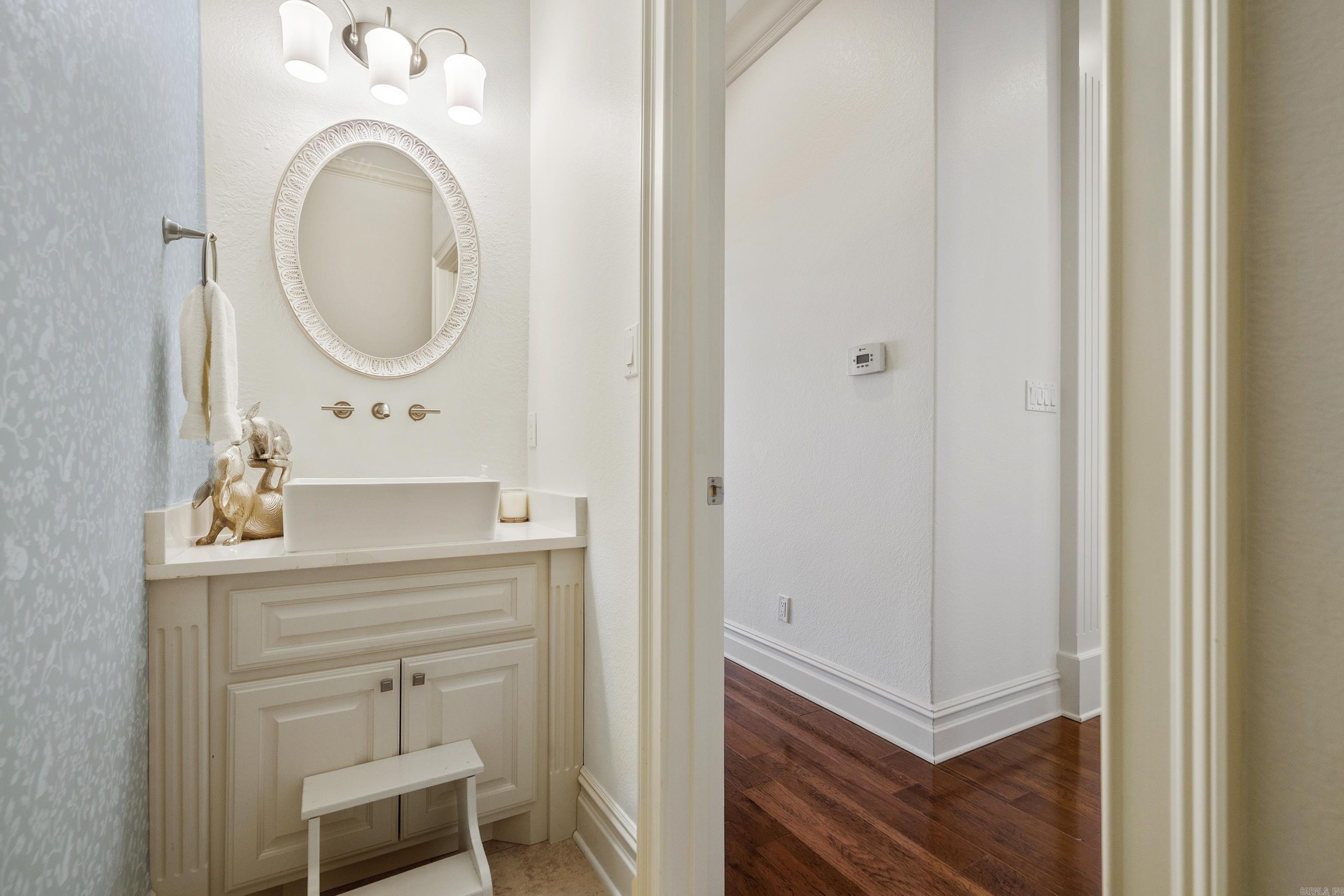 Bathroom vanity with a vessel sink, ornate oval mirror, and cream paneled cabinetry.
