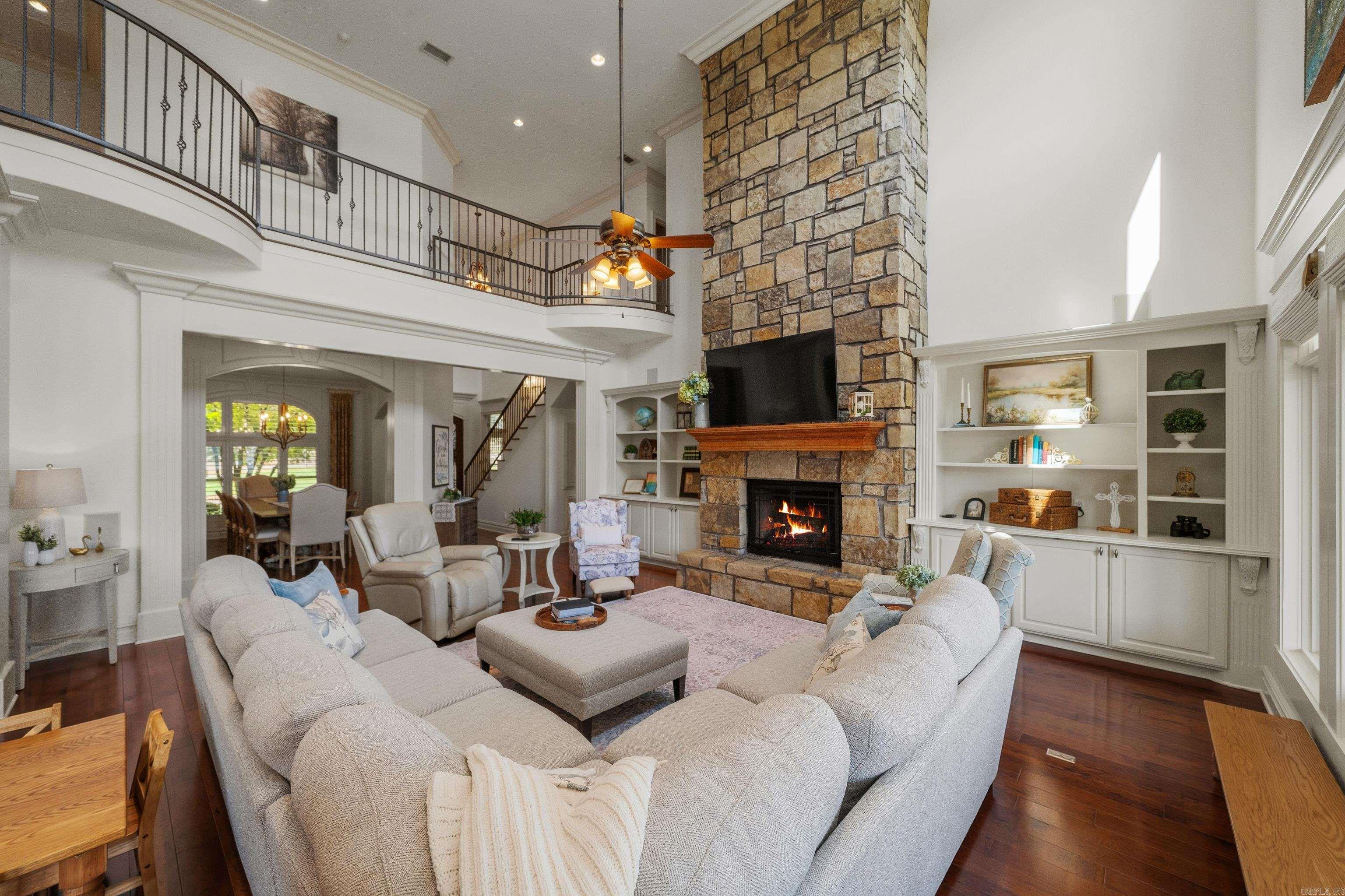Double-height living room with a stone fireplace, white built-ins, and an upper-level balcony.