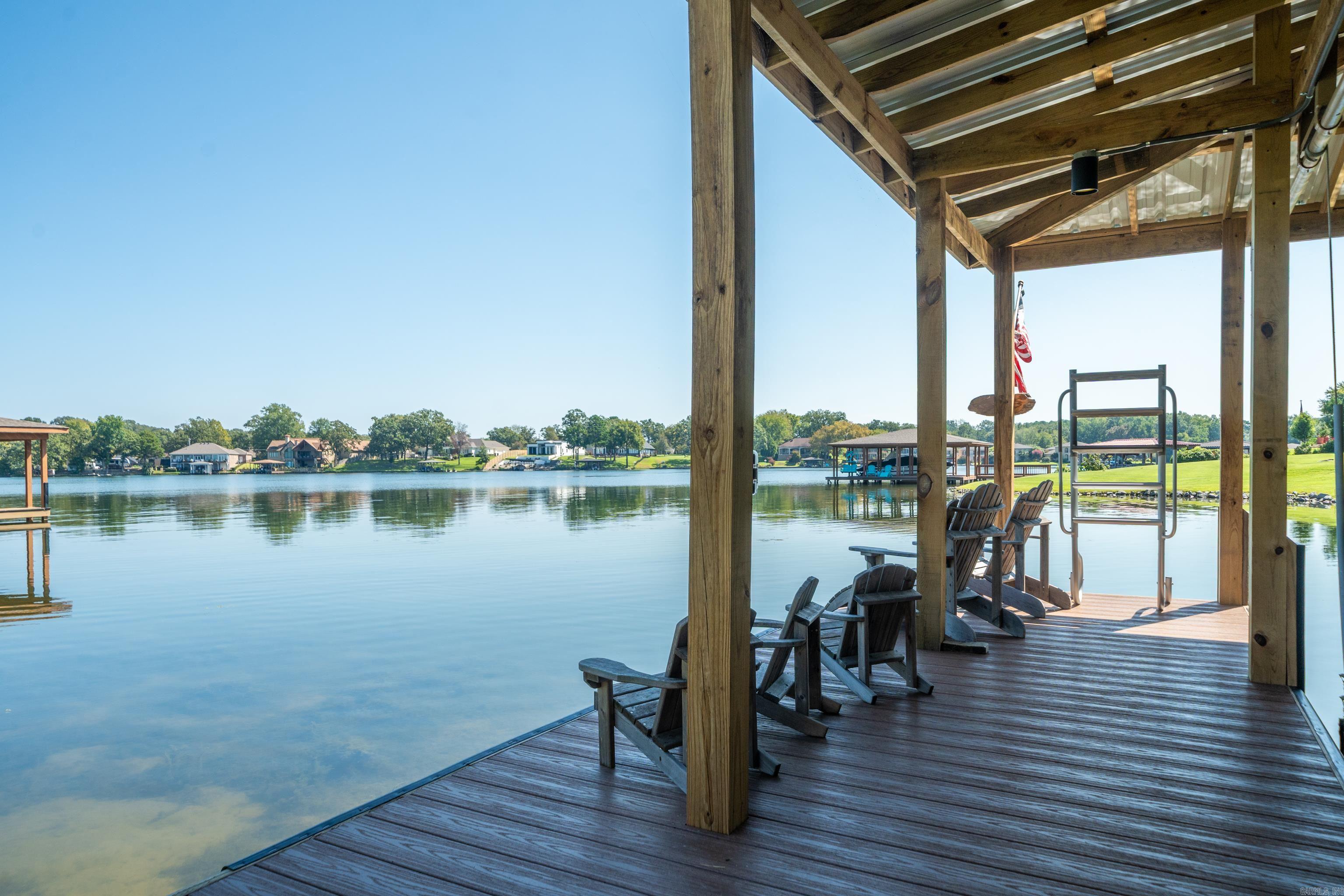 Covered lakeside dock with Adirondack chairs, a swim ladder, and a view across the water.