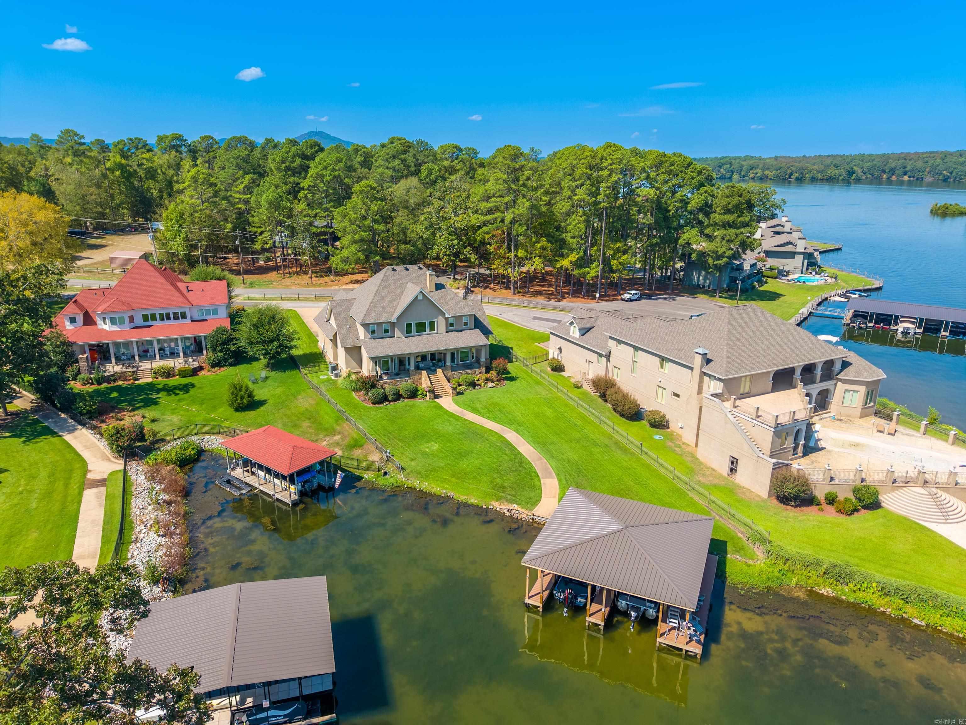 Aerial view of lakefront homes, covered docks, green lawns, and a wooded shoreline.