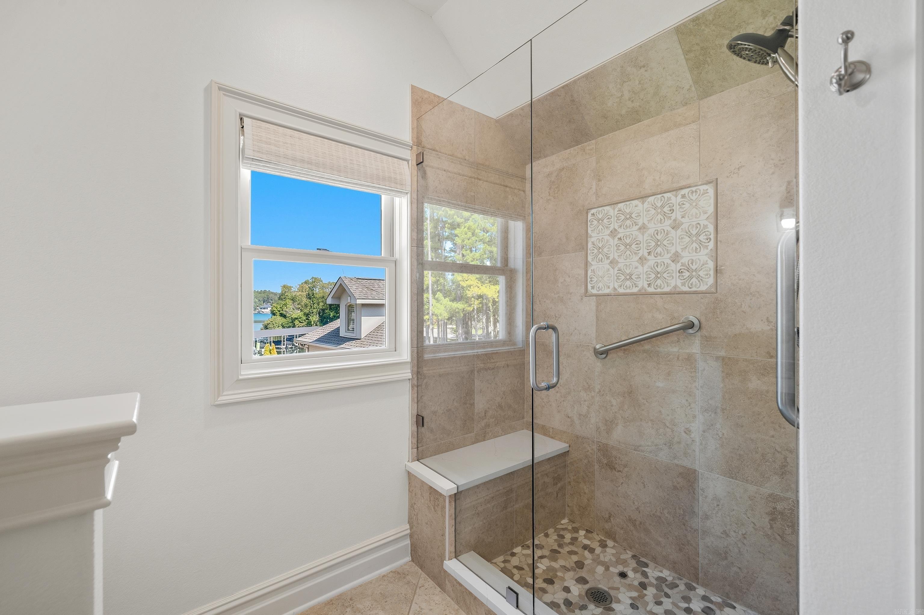 Bathroom with a glass walk-in shower, pebble floor, and window overlooking trees and water.
