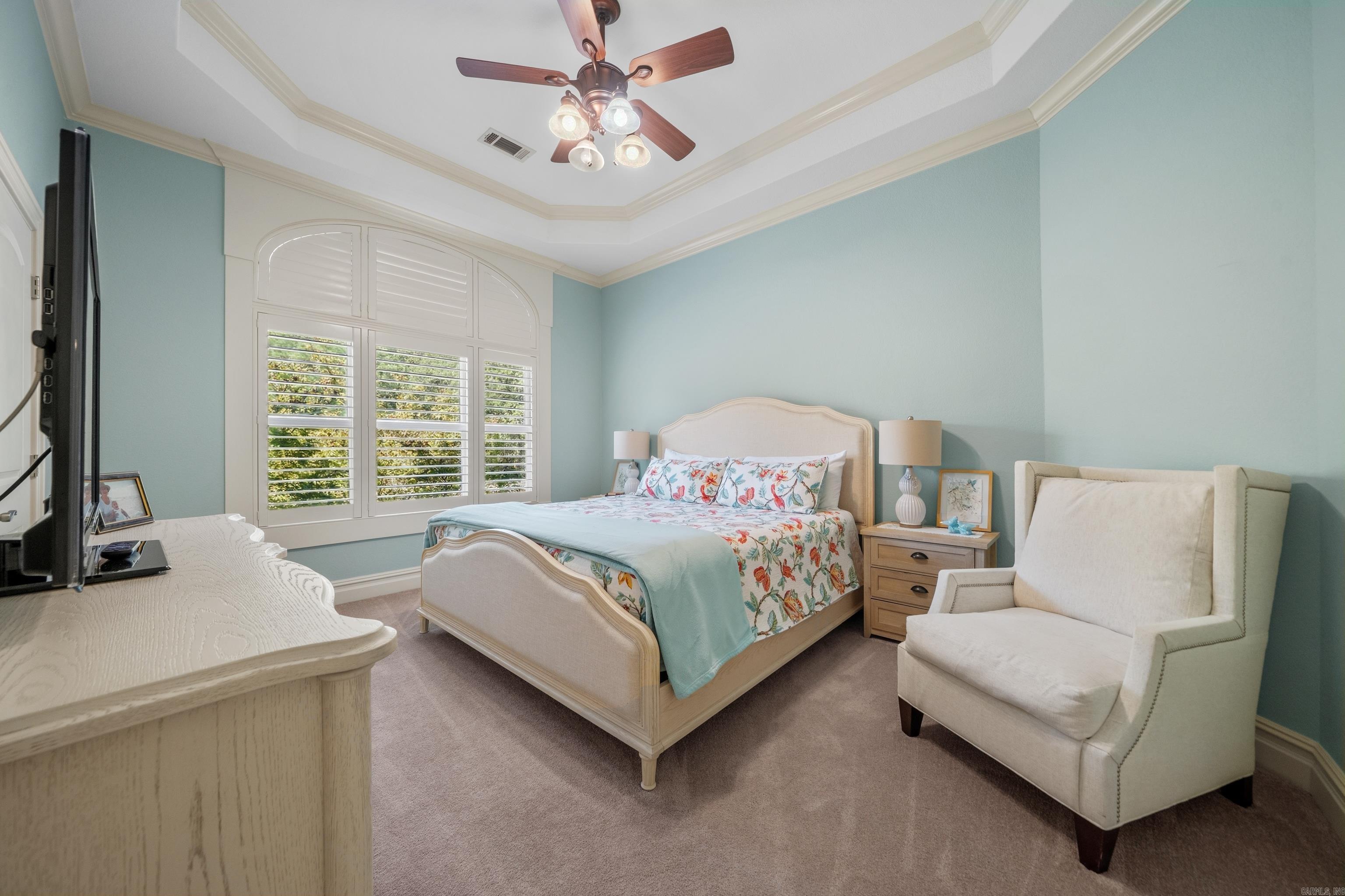 Bedroom with floral bedding, arched plantation shutters, and a white upholstered armchair.