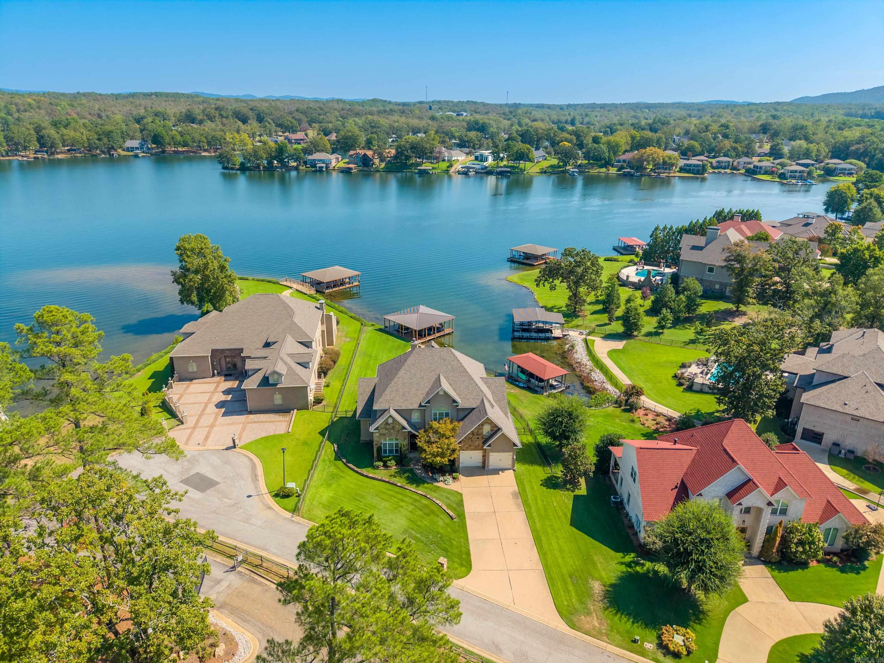 Aerial view of a lakeside neighborhood with waterfront homes, docks, and green lawns.