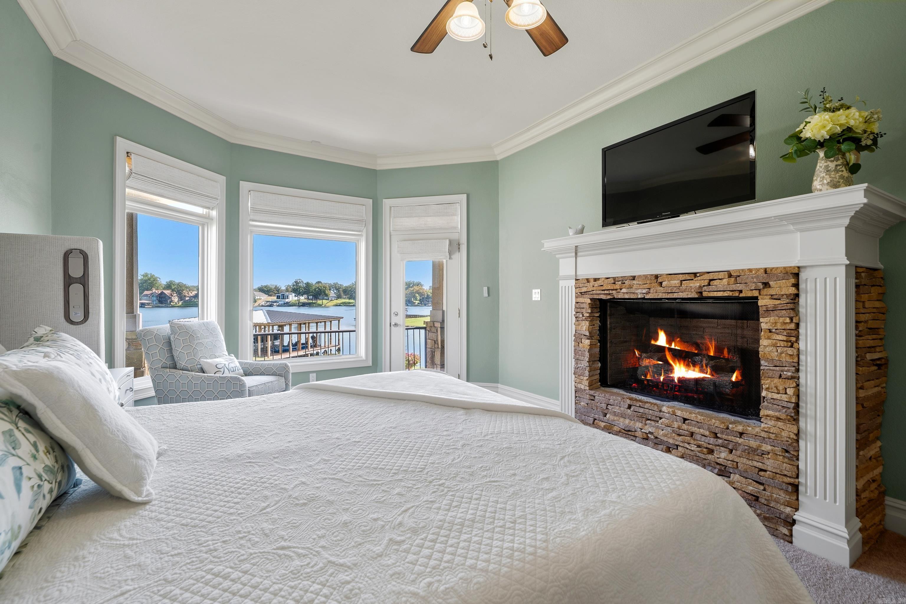 Bedroom with a stone fireplace, lake views, and a white quilted bed.