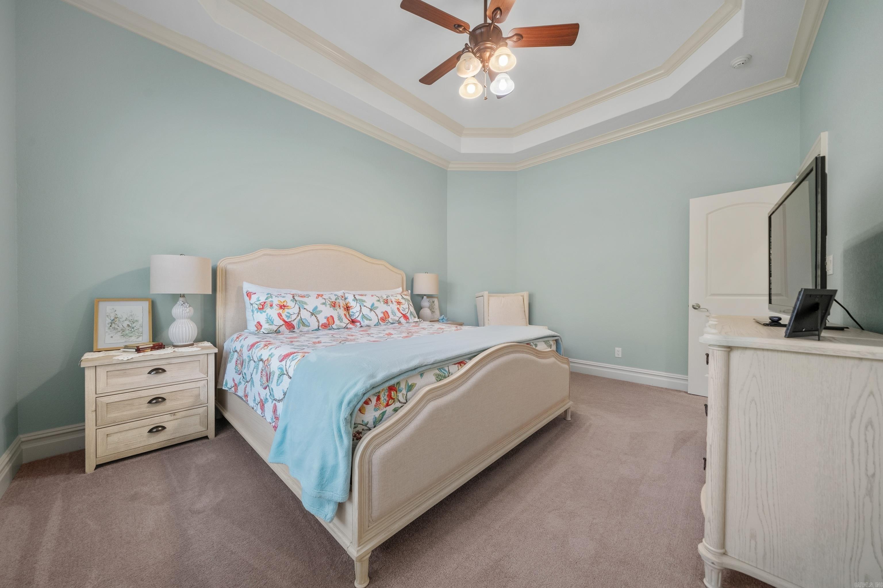 Furnished bedroom with a cream bed, colorful floral bedding, blue walls, and a tray ceiling.