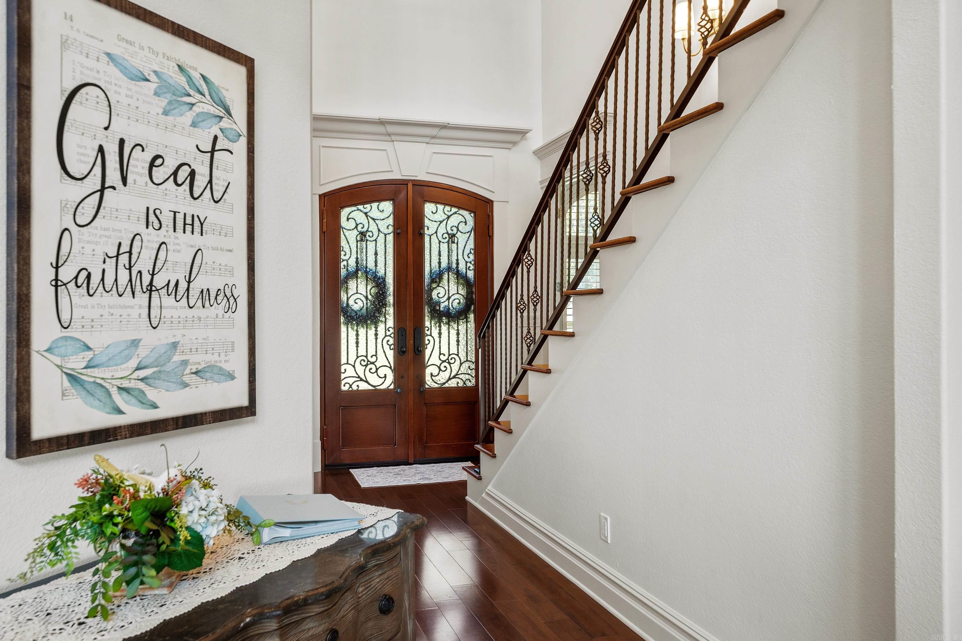 Foyer with ornate glass double doors, a curved staircase, and framed faithfulness artwork.