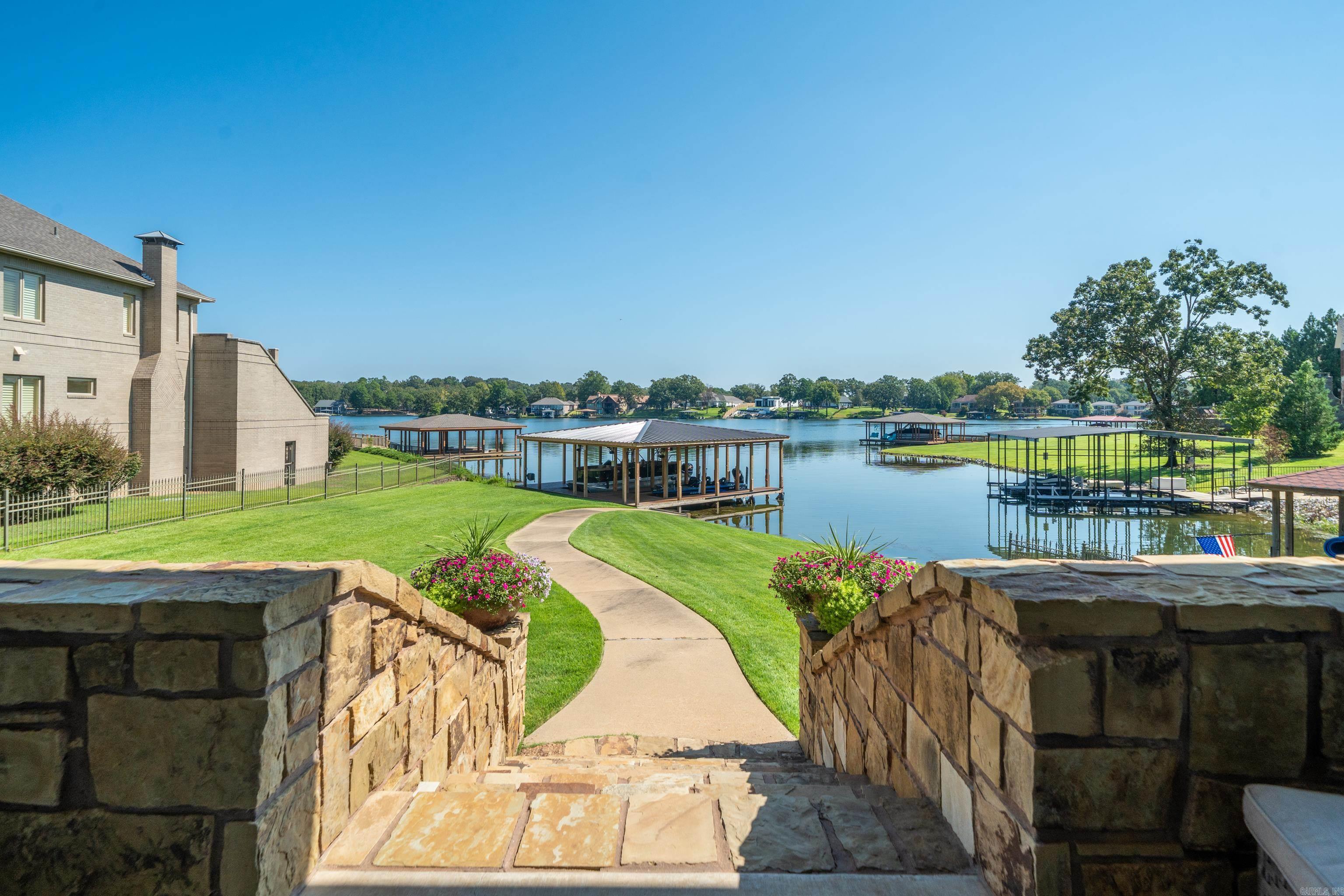 Stone steps lead across a green lawn to a lakeside dock, with covered boat slips on the water.