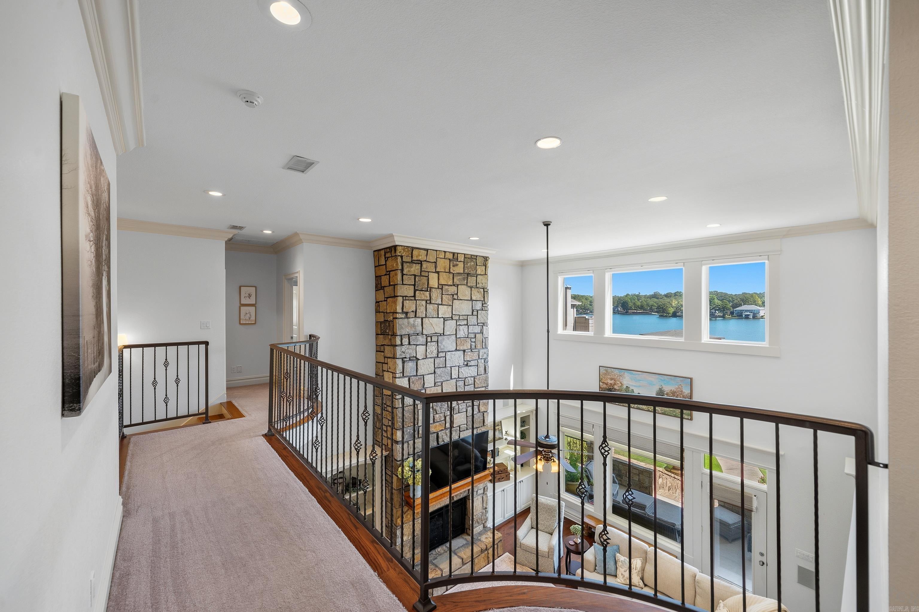 Upper-level landing overlooks a stone fireplace and furnished living room with lake views.