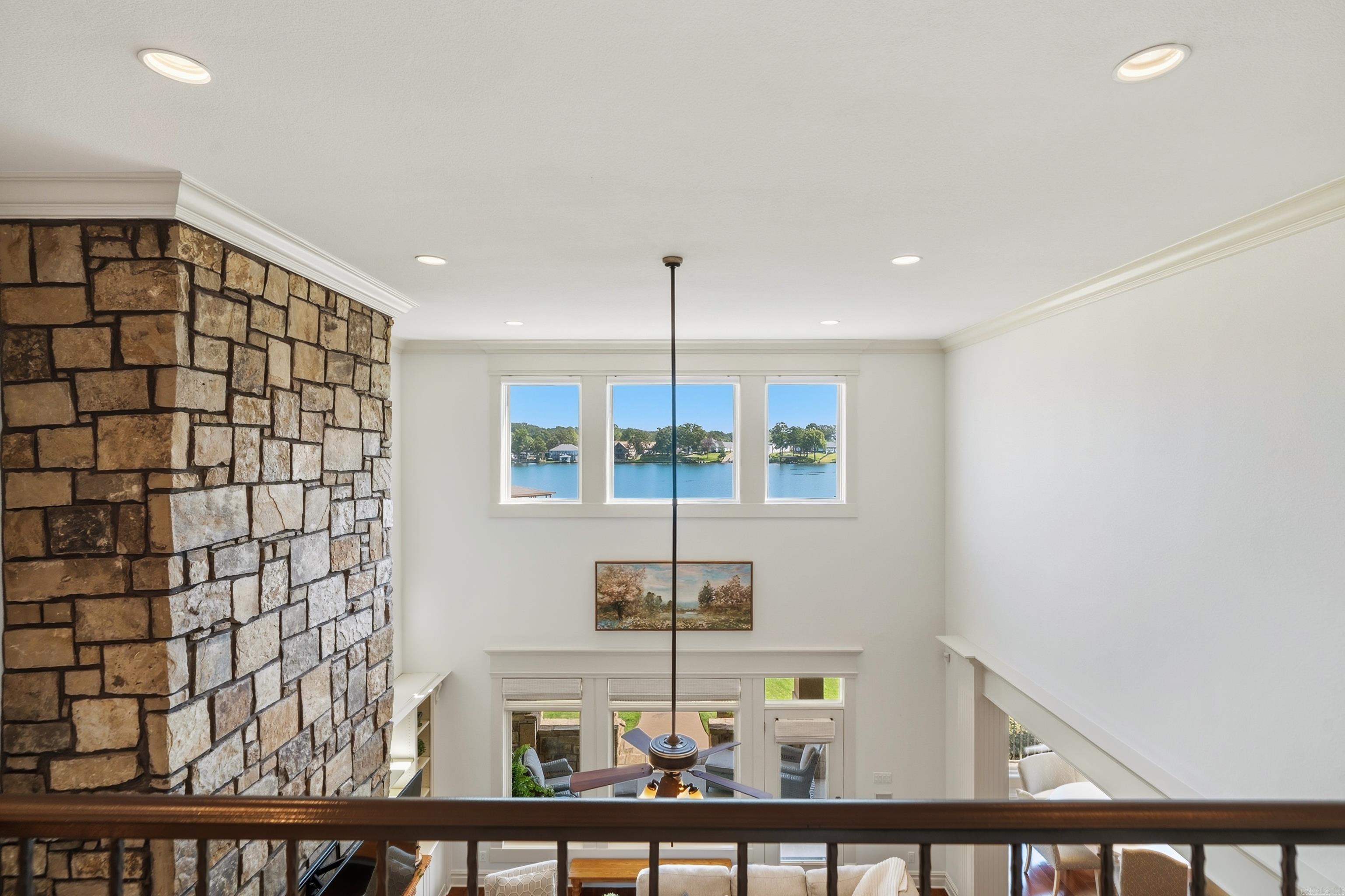 Two-story living room with a stone fireplace wall and lake views through three upper windows.