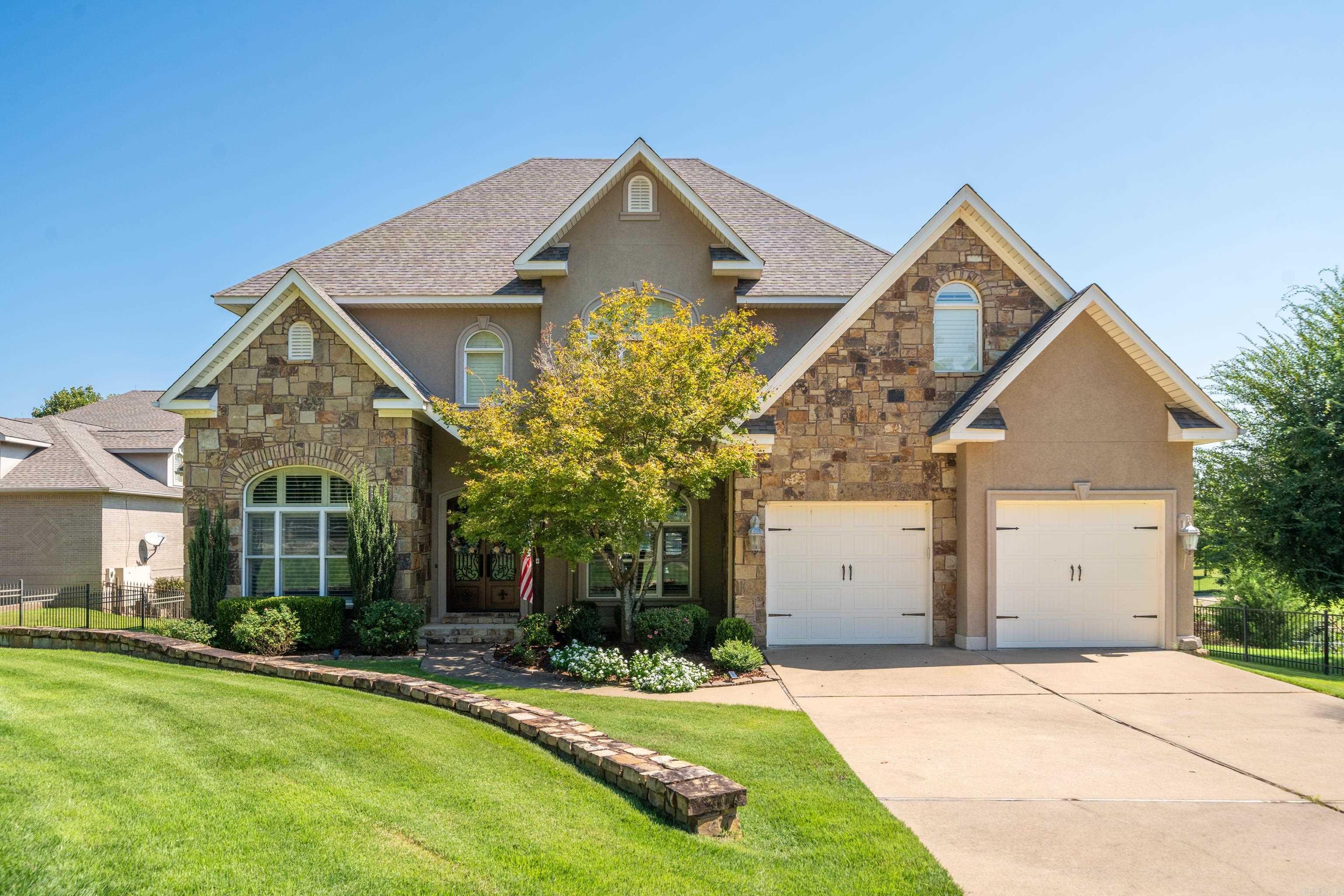 Two-story stone-and-stucco home with two garage doors, a covered entry, and landscaped lawn.