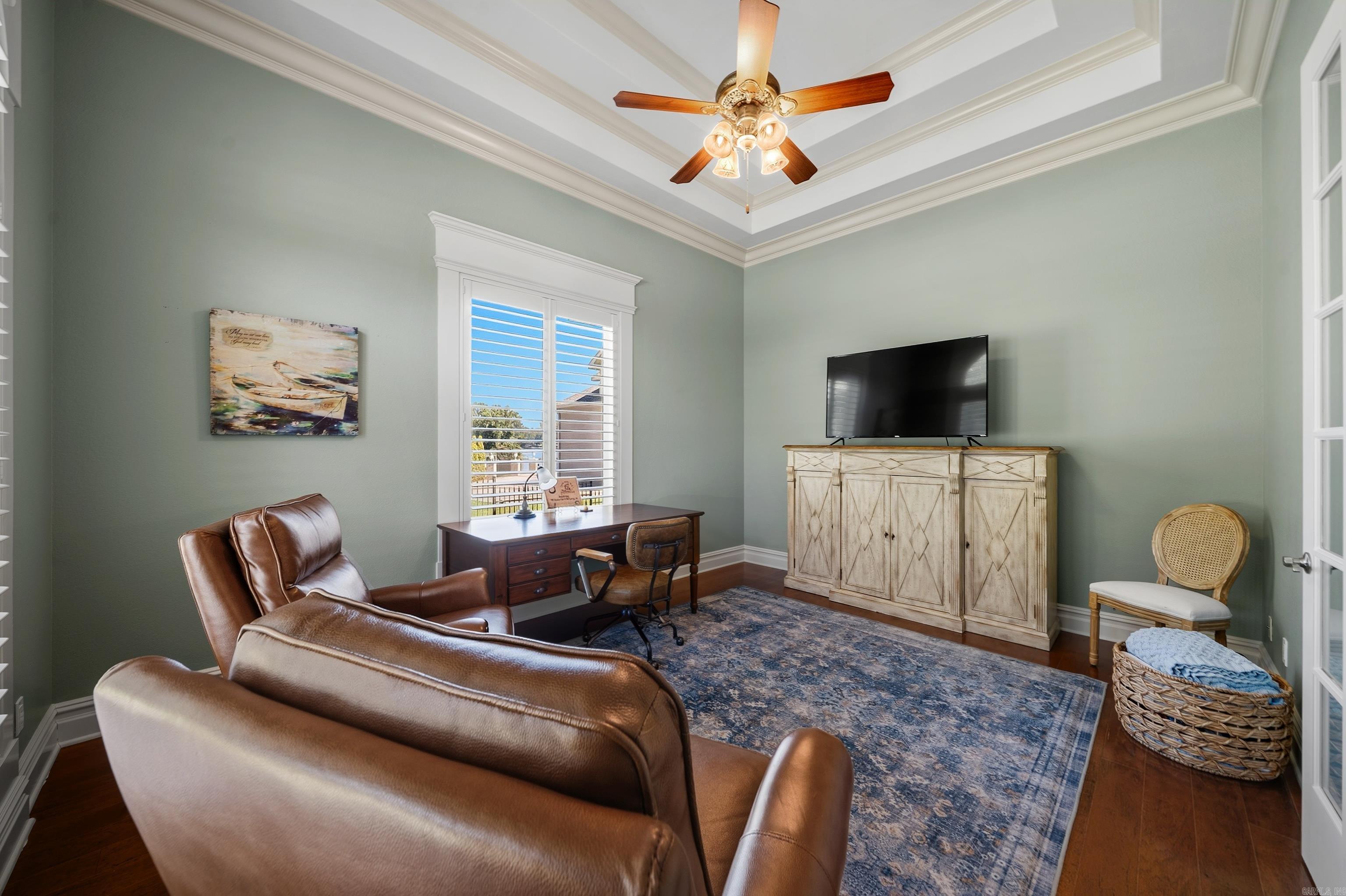 Furnished home office with a desk, leather seating, and a tray ceiling with a ceiling fan.
