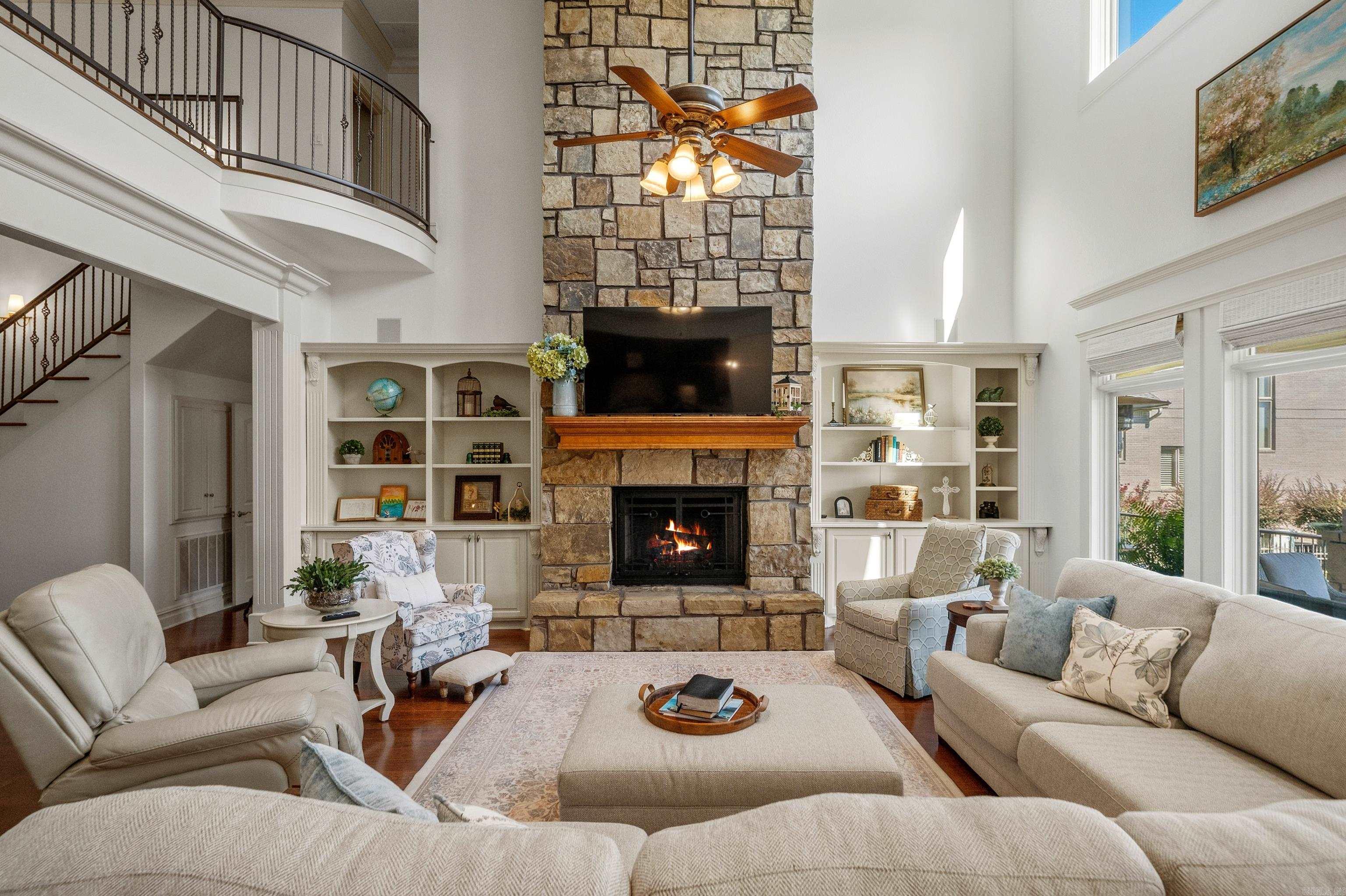 Living room with a soaring stone fireplace, built-in shelves, and curved staircase.